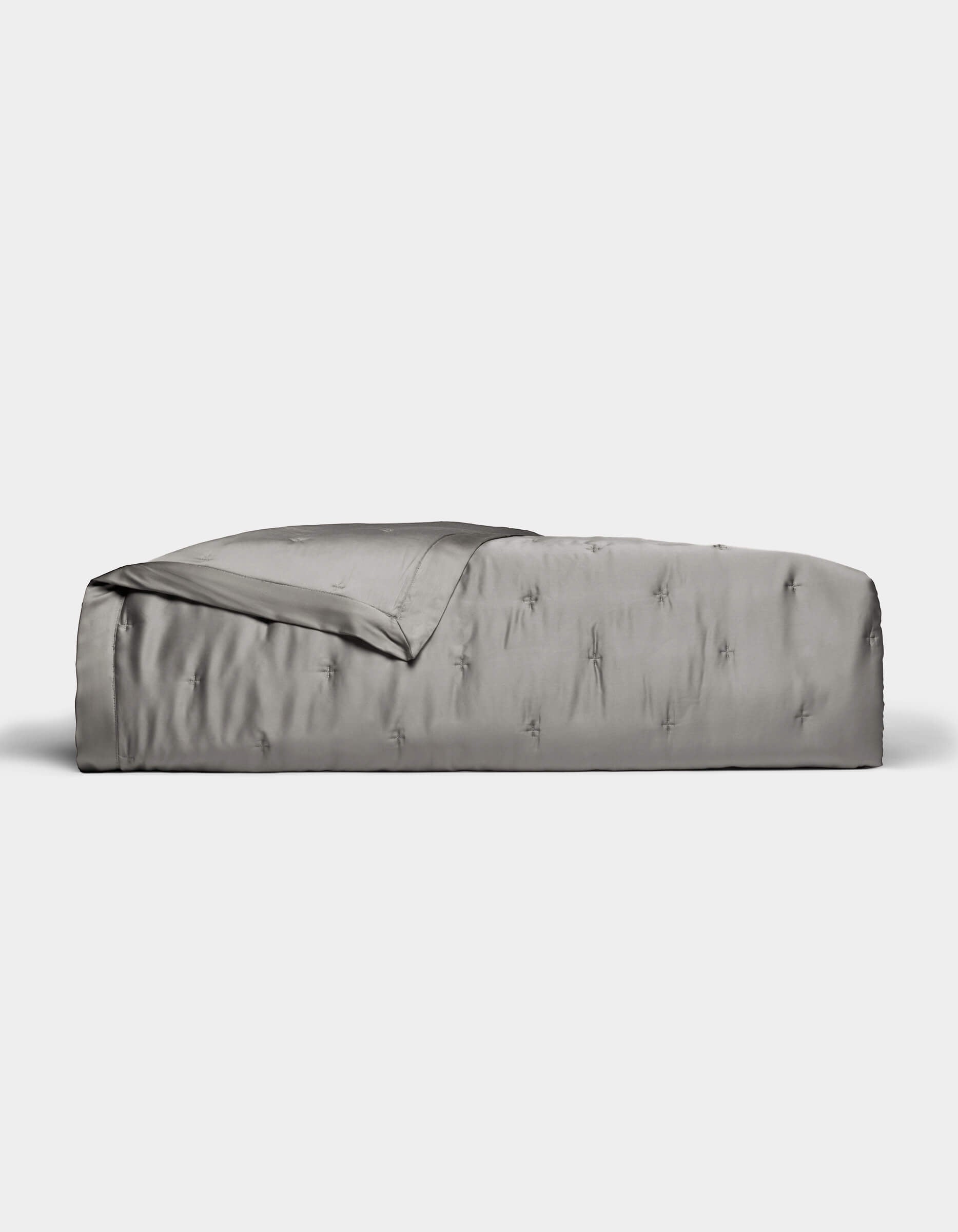 A neatly made bed features the Cozy Earth Bamboo Quilt in smooth, shiny silver-gray satin, partially folded back at the top, set against a plain white background.|Color:Charcoal