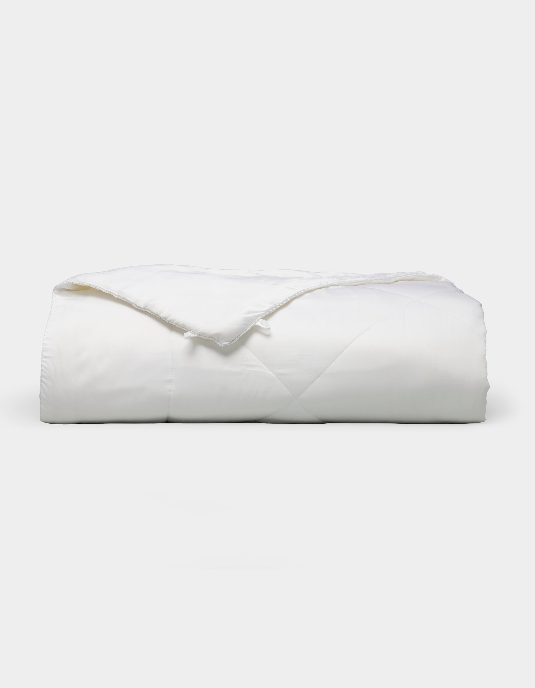 The Bamboo Viscose All Season Comforter by Cozy Earth, featuring a neatly folded white design with a subtle sheen, is displayed against a plain light background.|Filling:Standard