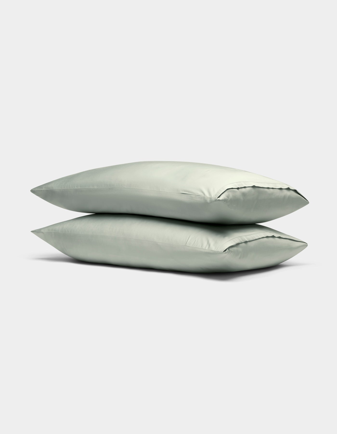 Two Cozy Earth Bamboo Pillowcases in light green are stacked neatly on top of each other against a plain, light gray background.|Color:Laurel