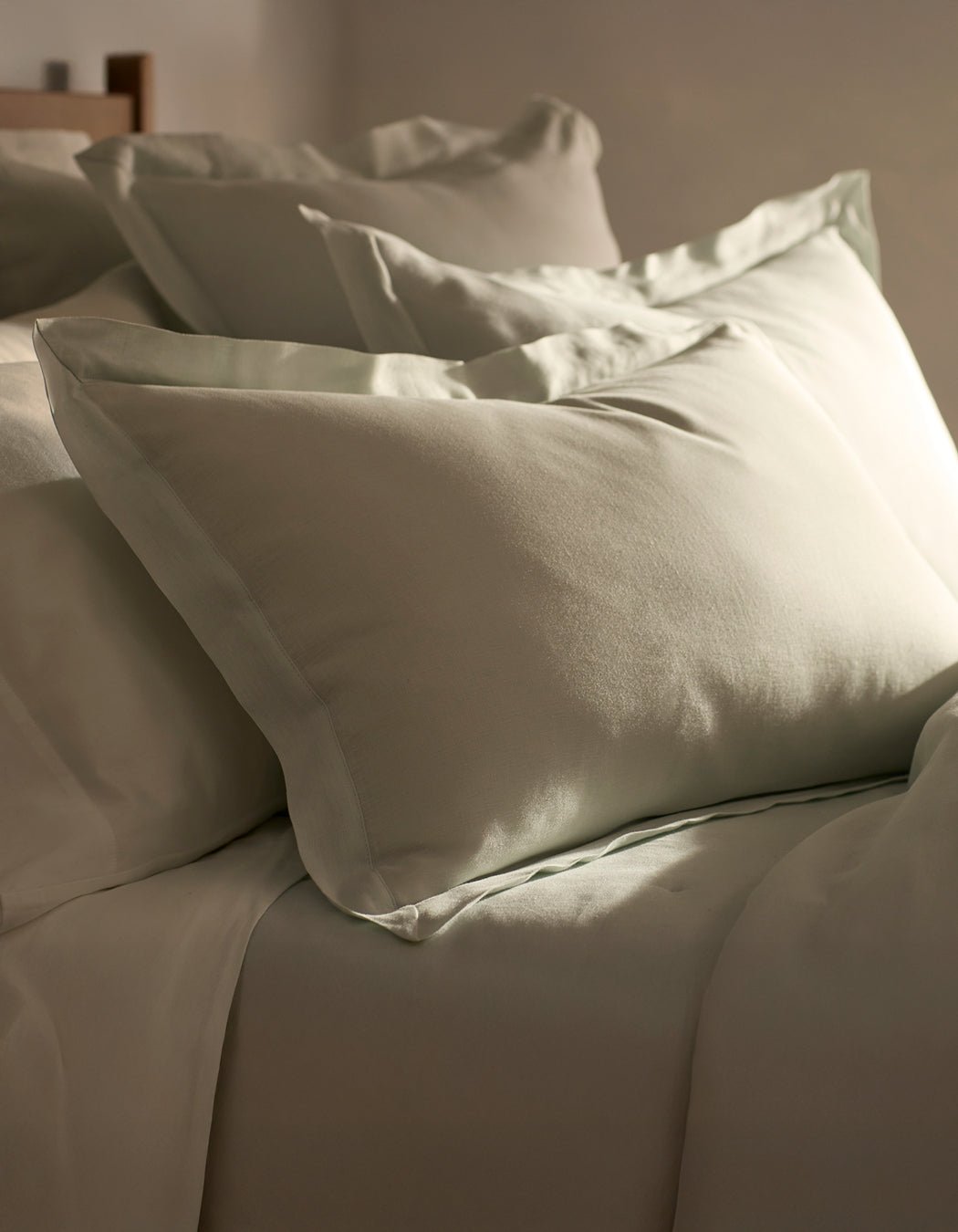 Cozy Earth Linen Shams are neatly arranged on a bed with light beige bedding, beautifully illuminated by soft natural light from the side.|Color:Mist