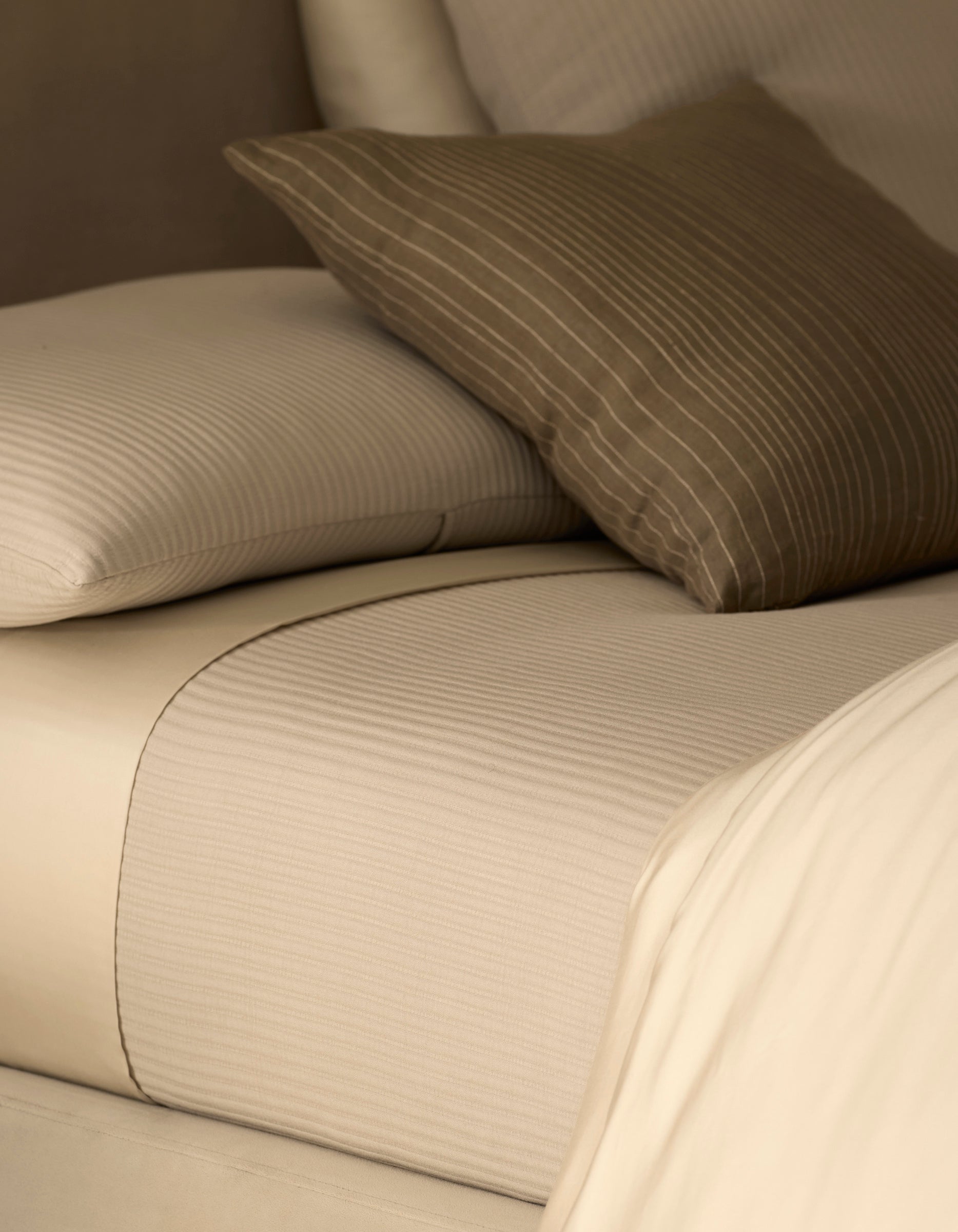 Close-up of beige bed sheets and pillows with a subtle pattern.
