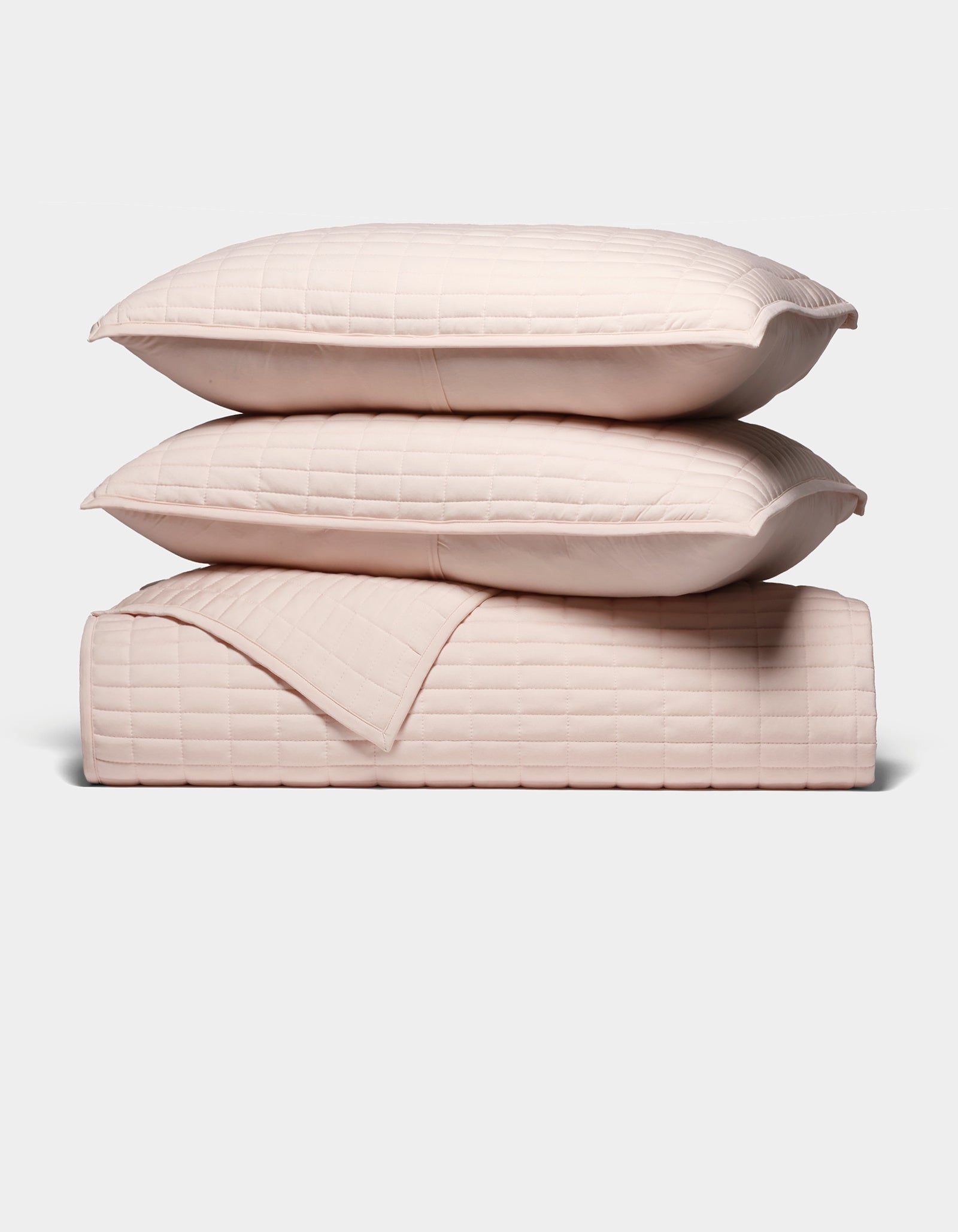 The Cozy Earth Bamboo Jersey Quilt Bundle features two light pink quilted pillows stacked atop a matching quilted blanket, all neatly arranged against a plain white background.|Color:Petal