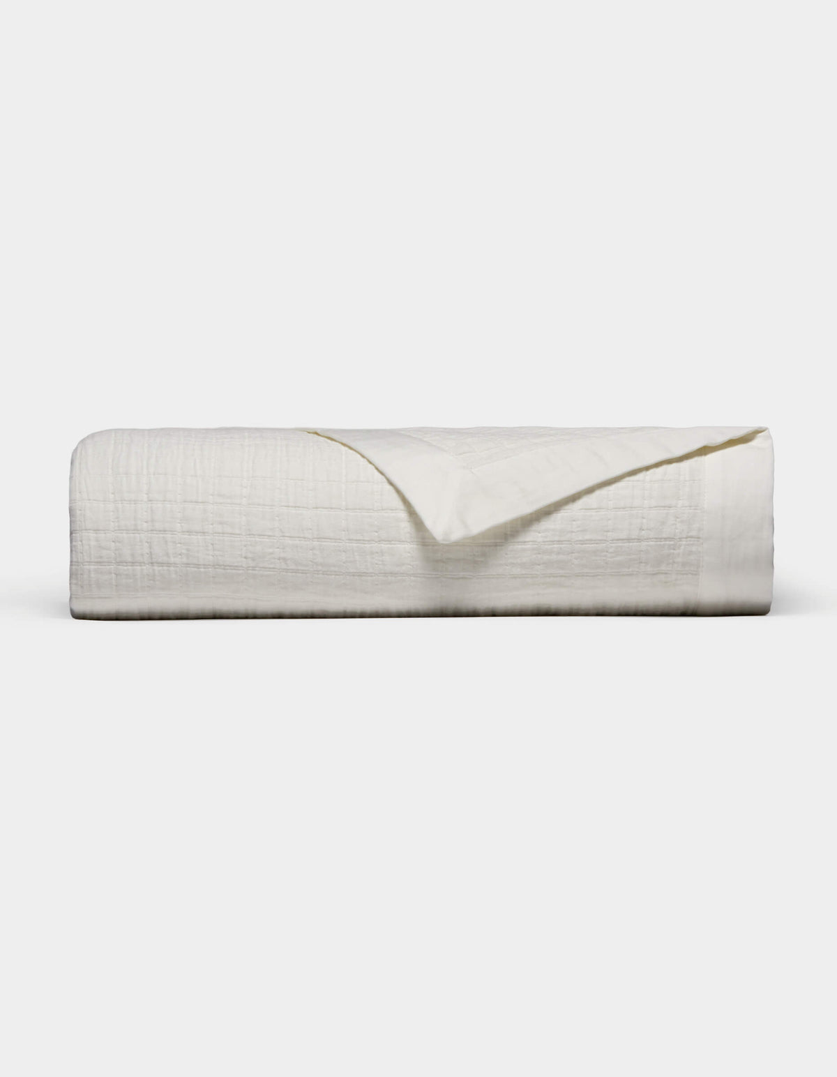 The Waterfront Grid Matelasse Blanket by Cozy Earth is shown neatly folded with a textured, crinkled surface against a plain light background. One corner is flipped over to reveal the underside.|Color:Sea Salt