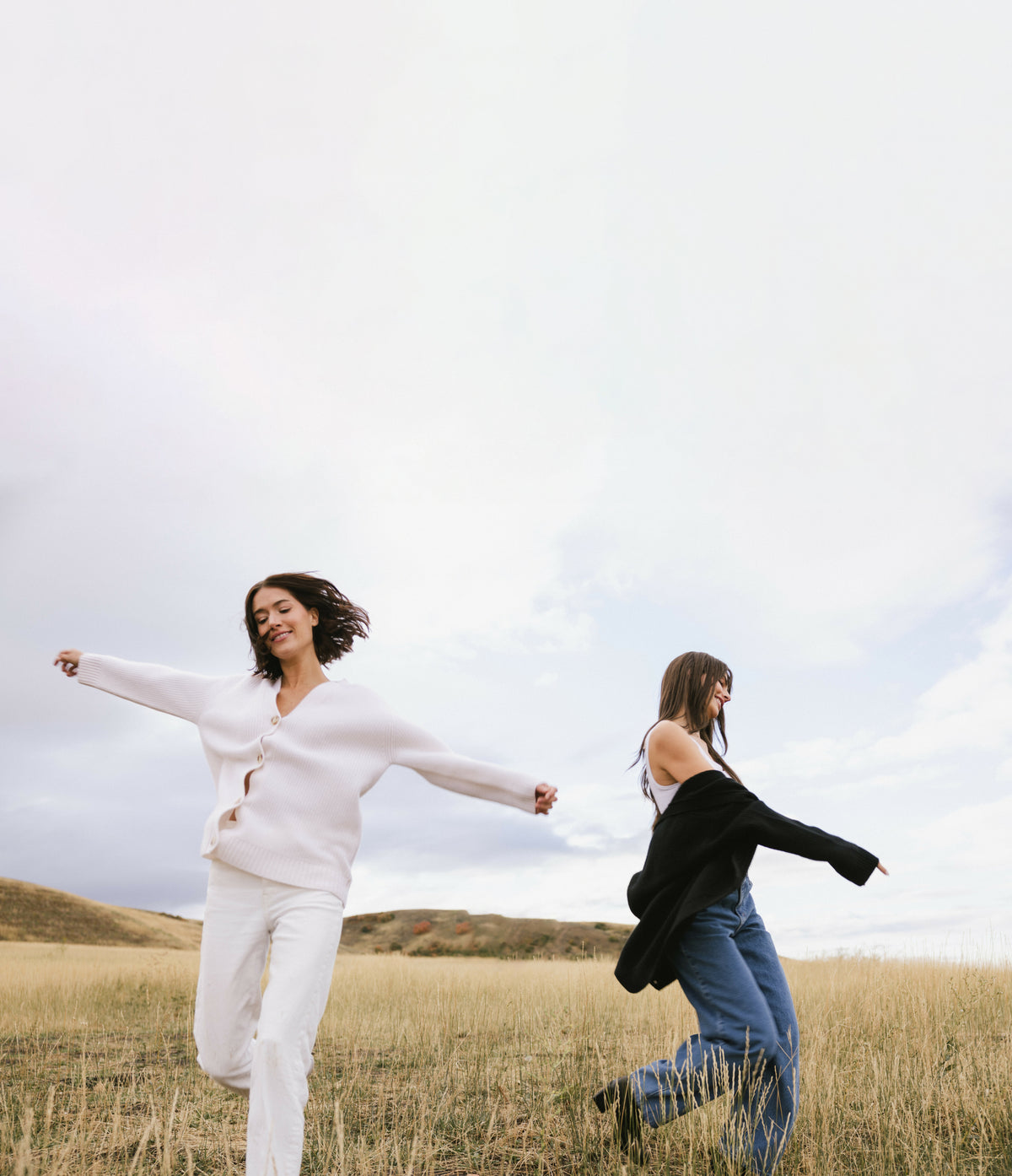 Two women running in a field with a clear sky