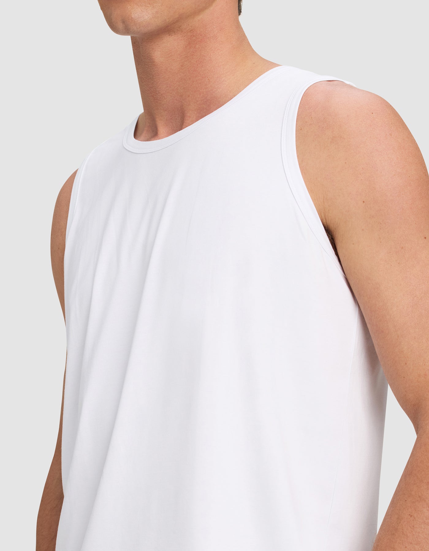 A person is shown from shoulders to waist wearing the Cozy Earth Men's First Layer Pajama Tank in white against a plain light gray background, with their face partially out of frame.|Color:White