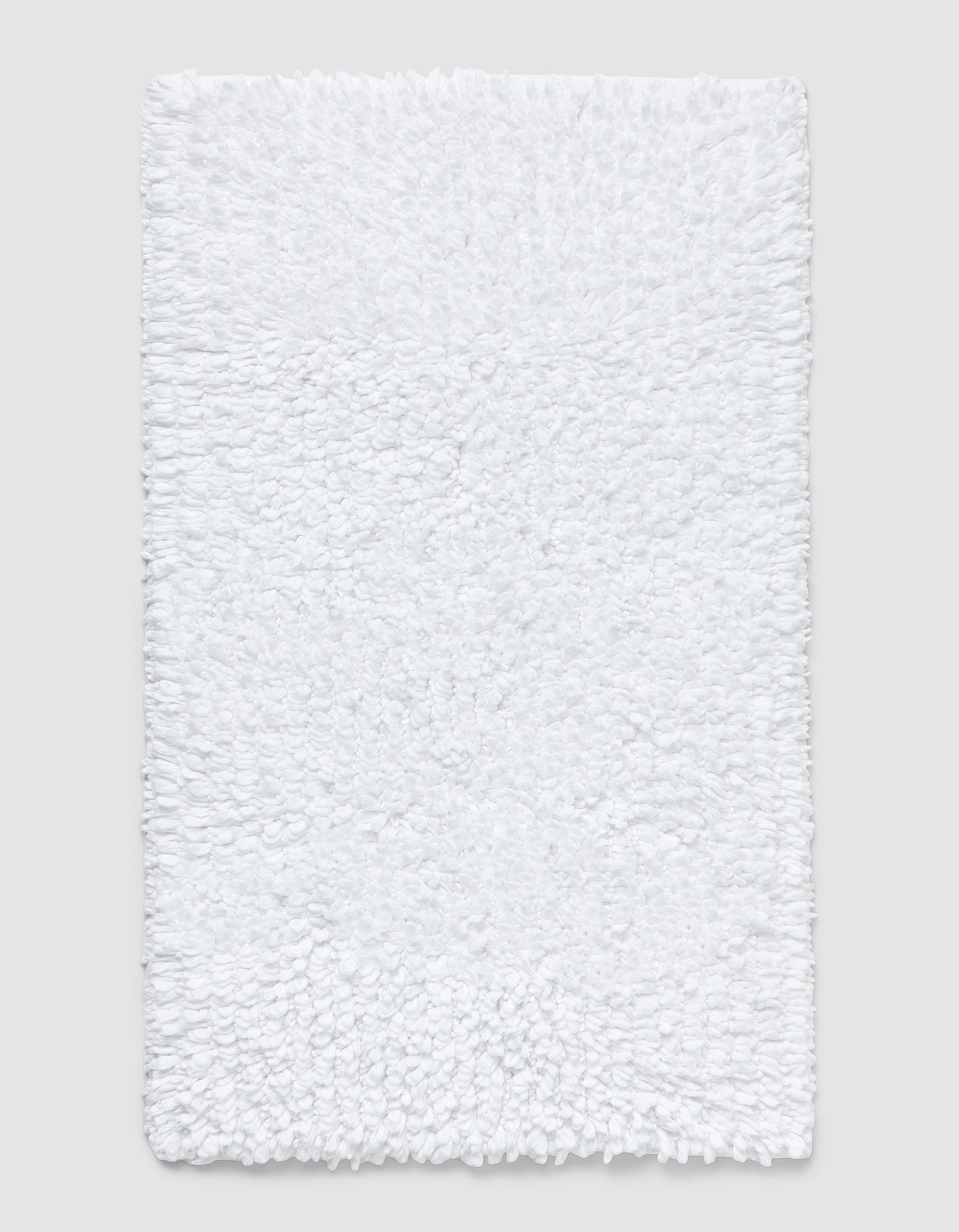 The Cozy Earth Plush Loop Bath Mat is rectangular, white, and features a soft, fluffy chenille shag texture. Shown on a plain light background, it offers plush comfort with its textured surface.|Color:White
