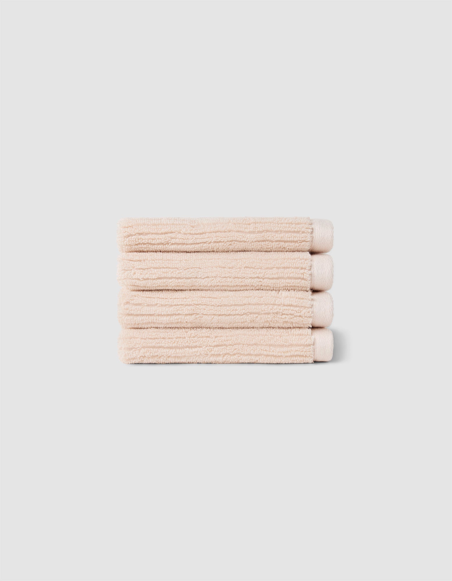 The Complete Ribbed Terry Bath Bundle by Cozy Earth features four neatly folded beige towels stacked atop each other against a plain light gray background.|Color:Petal