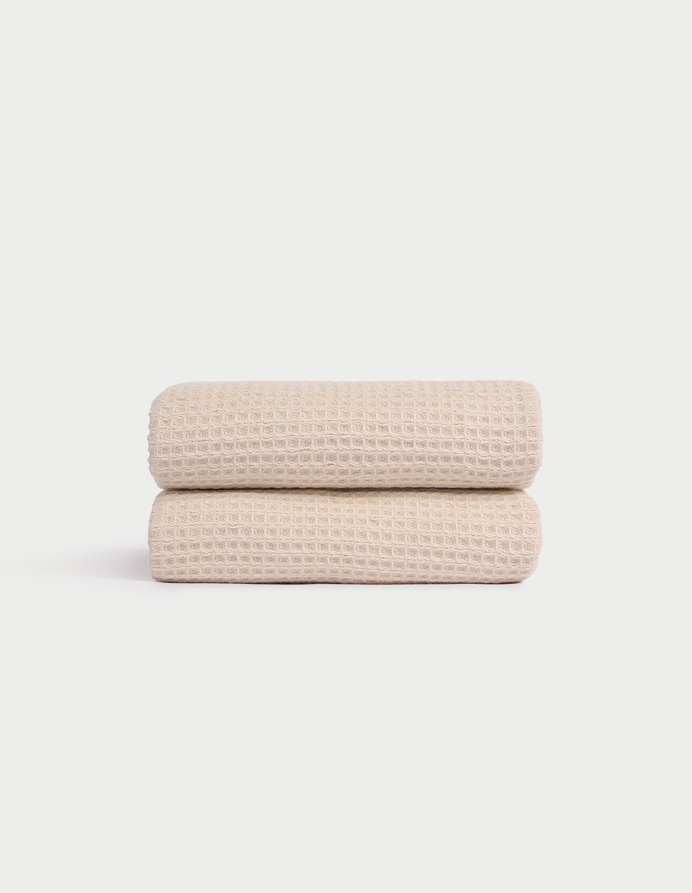 Two Cozy Earth Waffle Hand Towels in light beige are neatly folded and stacked against a plain white background, showcasing their textured pattern. |Color:Birch
