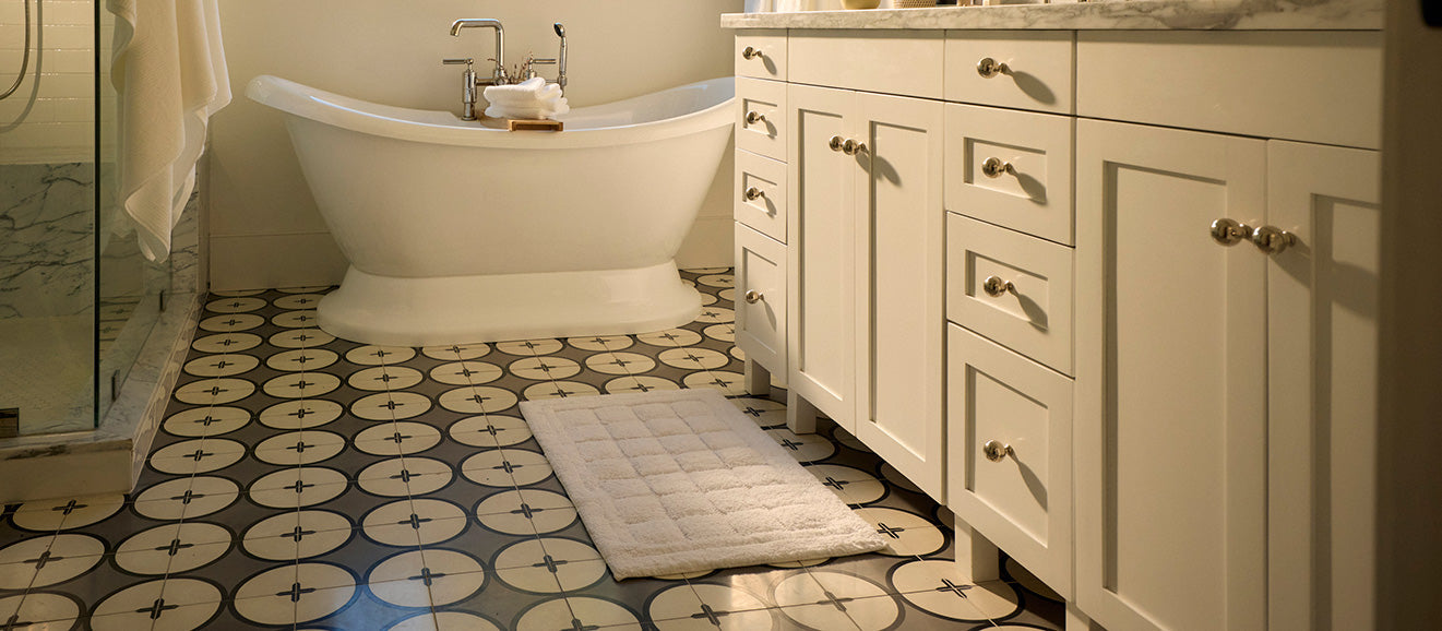 a bathroom with circular tile pattern, white tub, vanity, and white bath mat