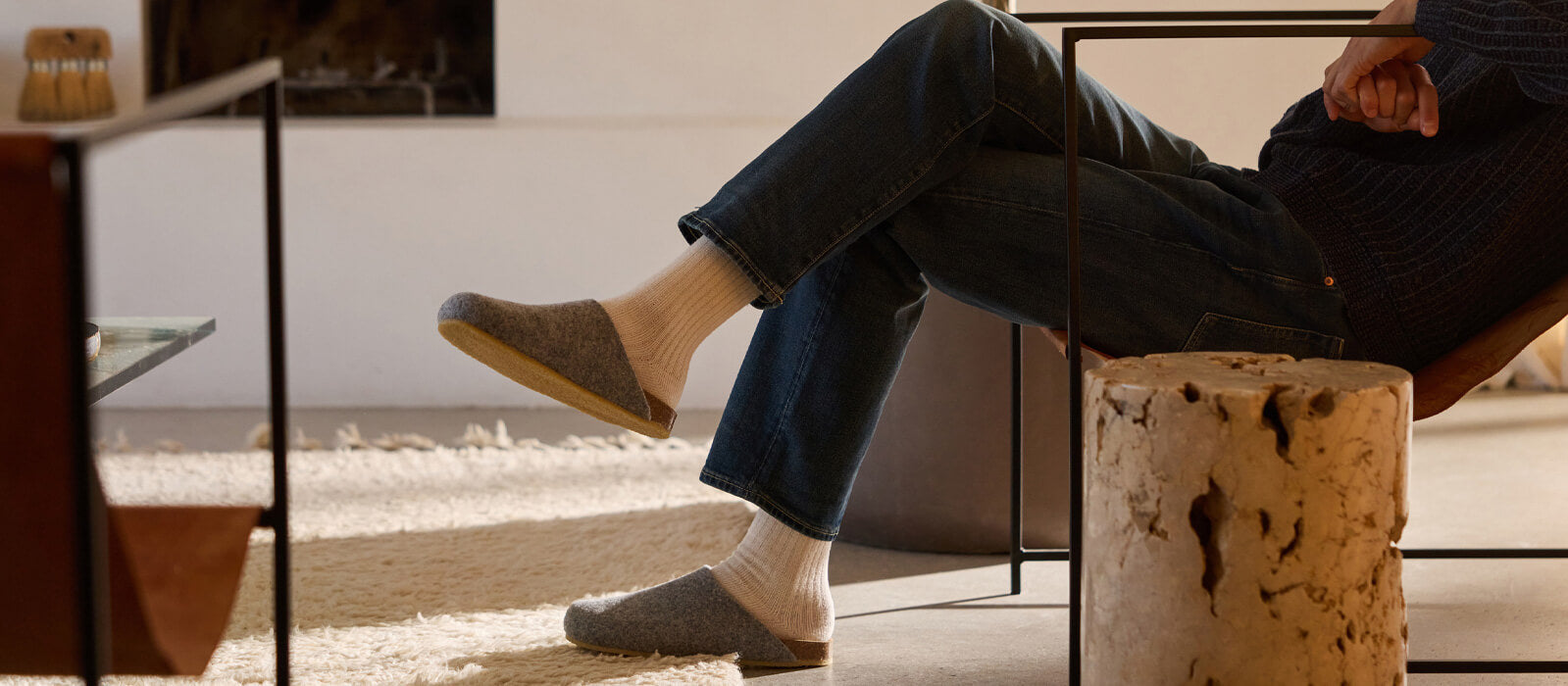 A man wearing jeans sits in a chair. He wears Cozy Earth Lakhouse Clogs