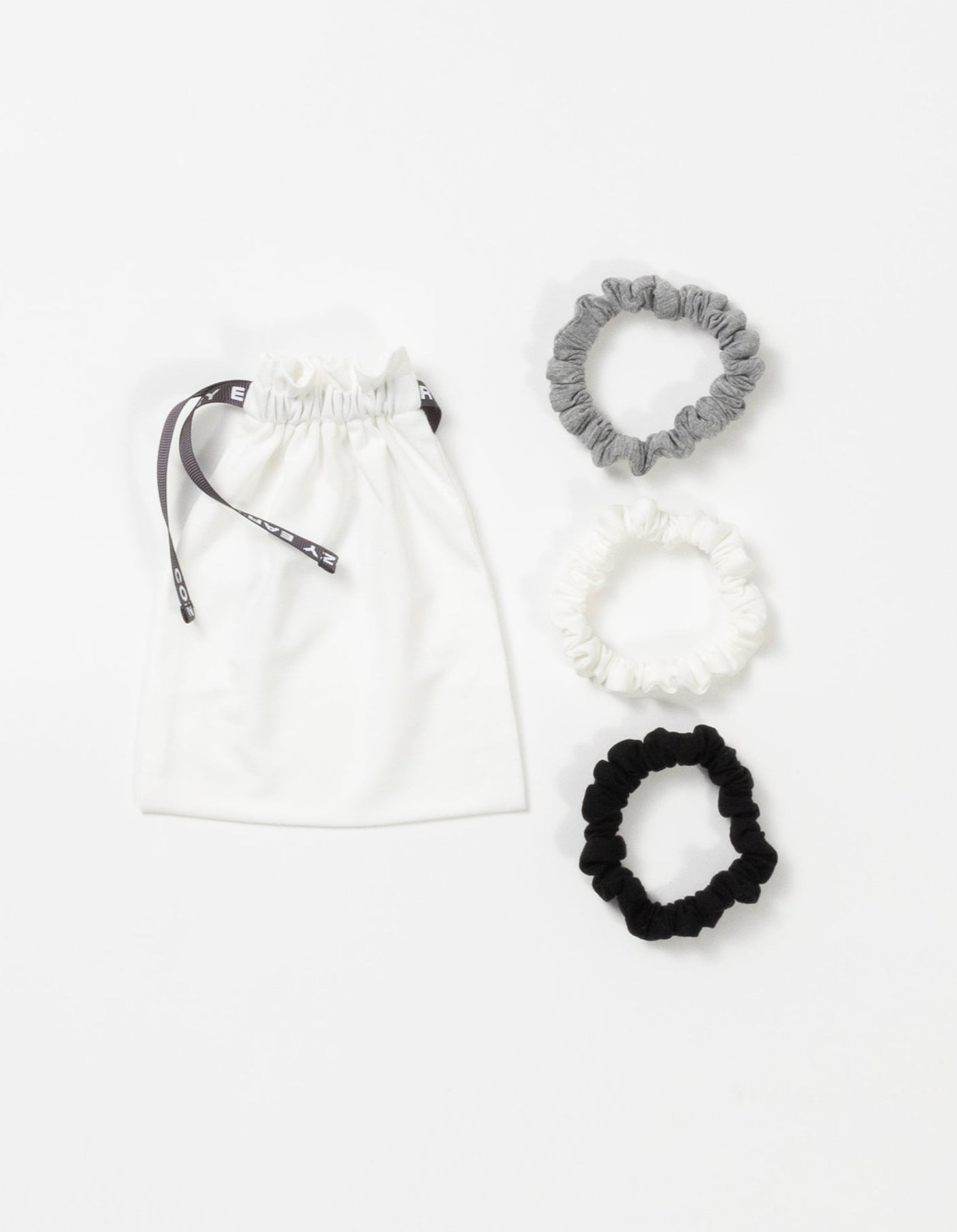 Cozy Earth Bamboo Stretch Knit Skinny Scrunchies in Grey, Ivory, and Black pictured with storage bag on a white background. 
