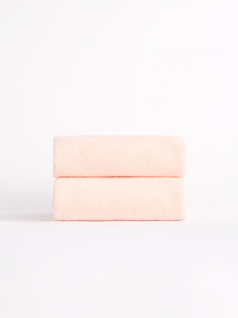 Two Luxe Hand Towels by Cozy Earth, in a soft pink hue, neatly folded and stacked against a white background.