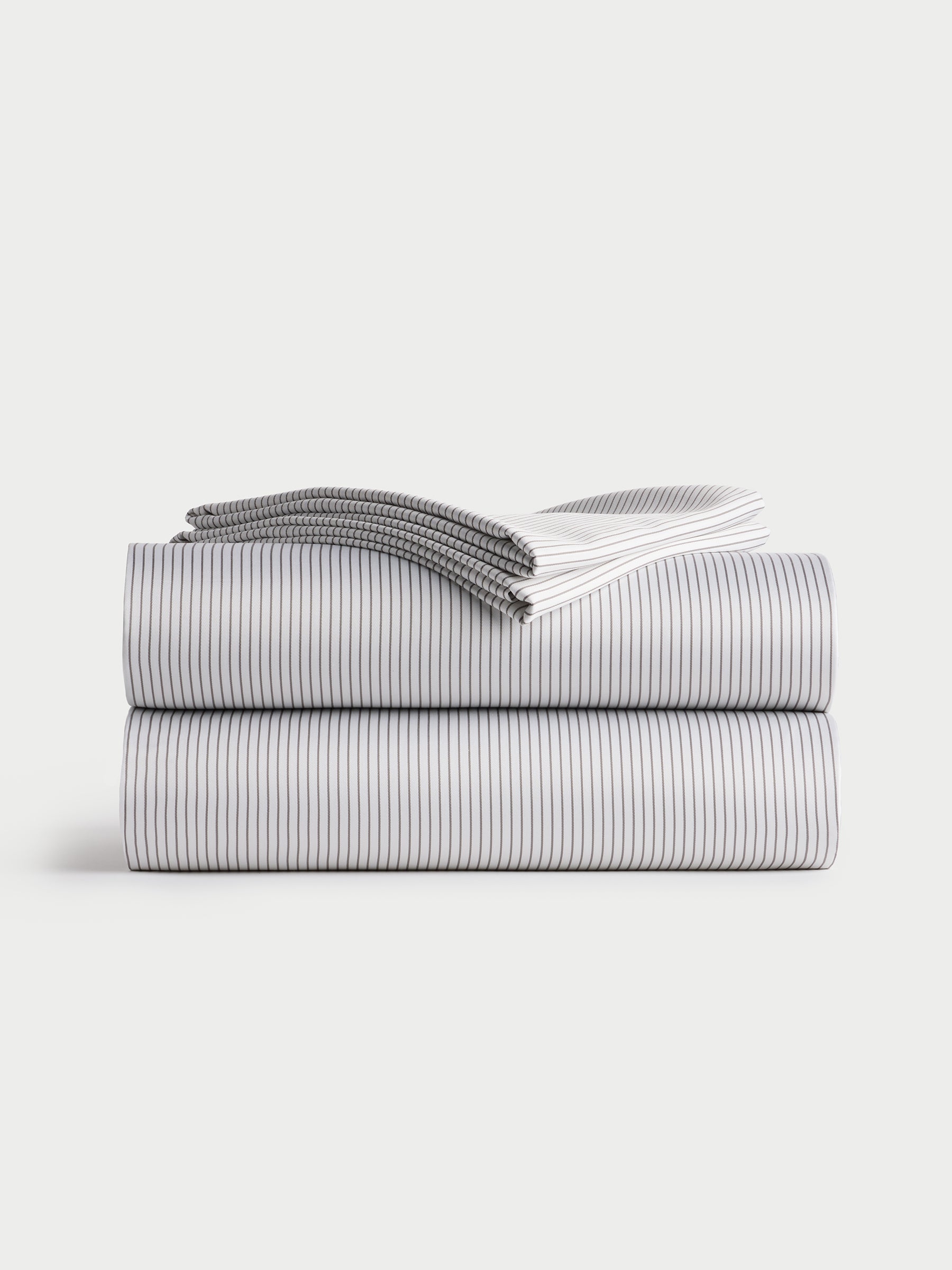 A neatly folded stack of Bamboo Sheet Sets from Cozy Earth, featuring a subtle black and white striped pattern. The sheets are arranged in a minimalist style on a plain white background. 