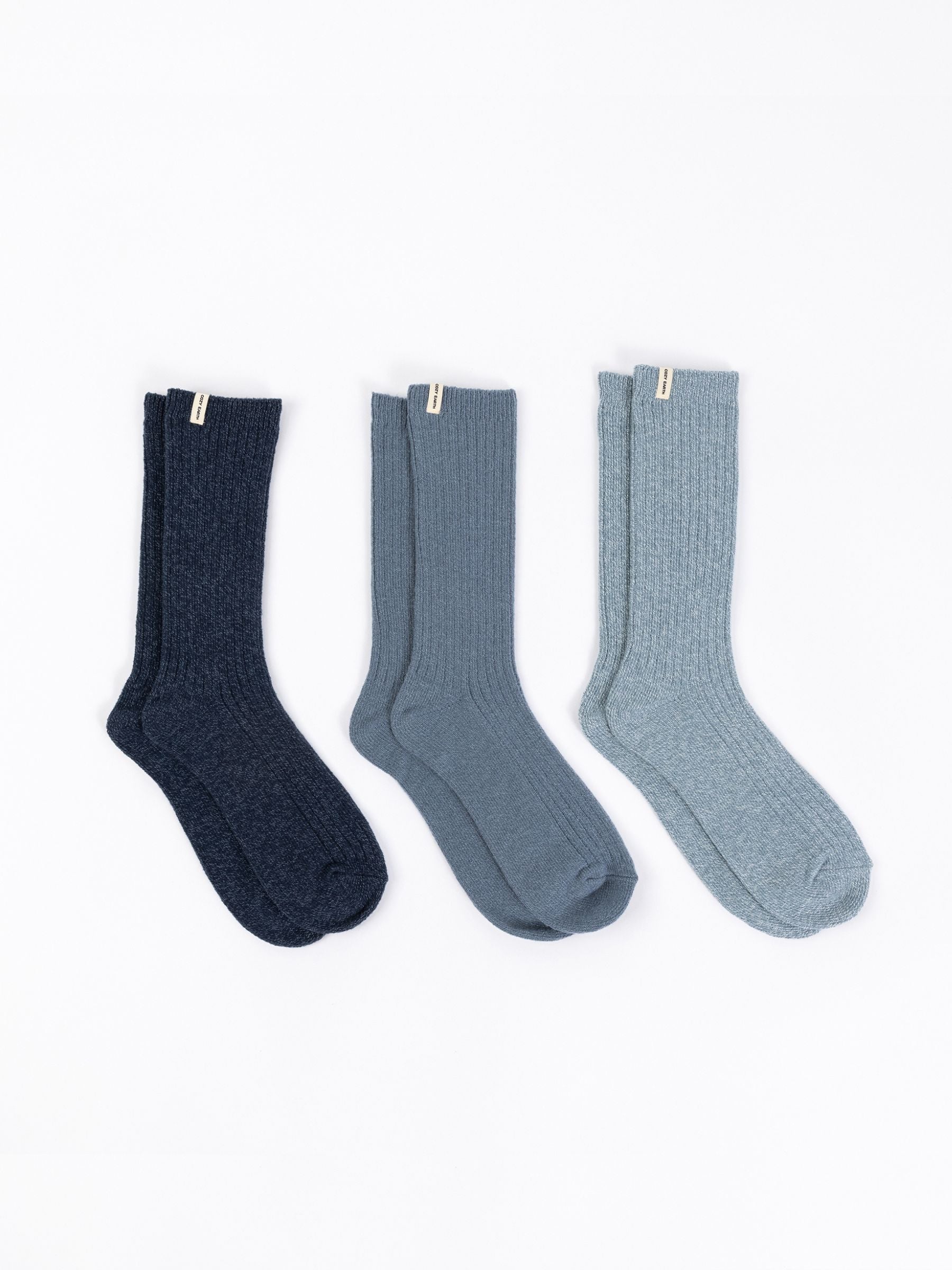 A set of The Plush Lounge Calf Sock 3-Pack by Cozy Earth, featuring three pairs in various blue tones, is stylishly displayed on a white background, each with a small tag near the cuff. 