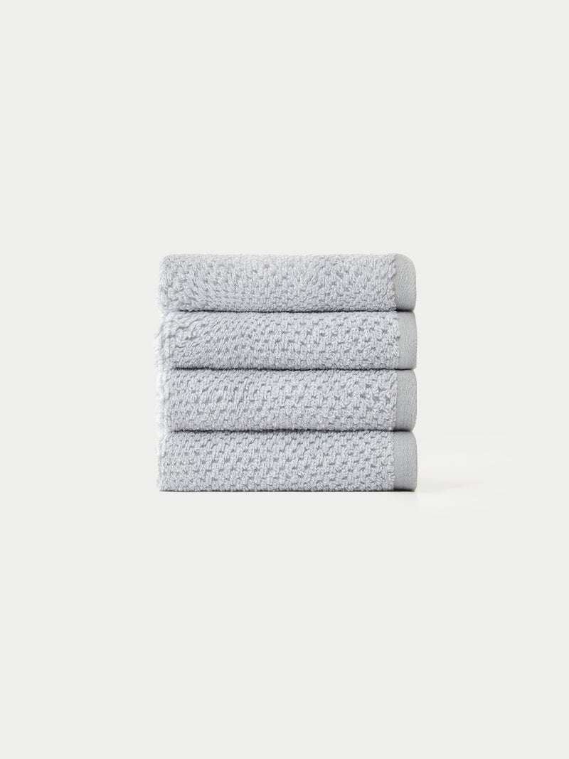 A neatly stacked pile of four light gray, textured towels from the Cozy Earth Nantucket Bath Towel Set on a plain white background.