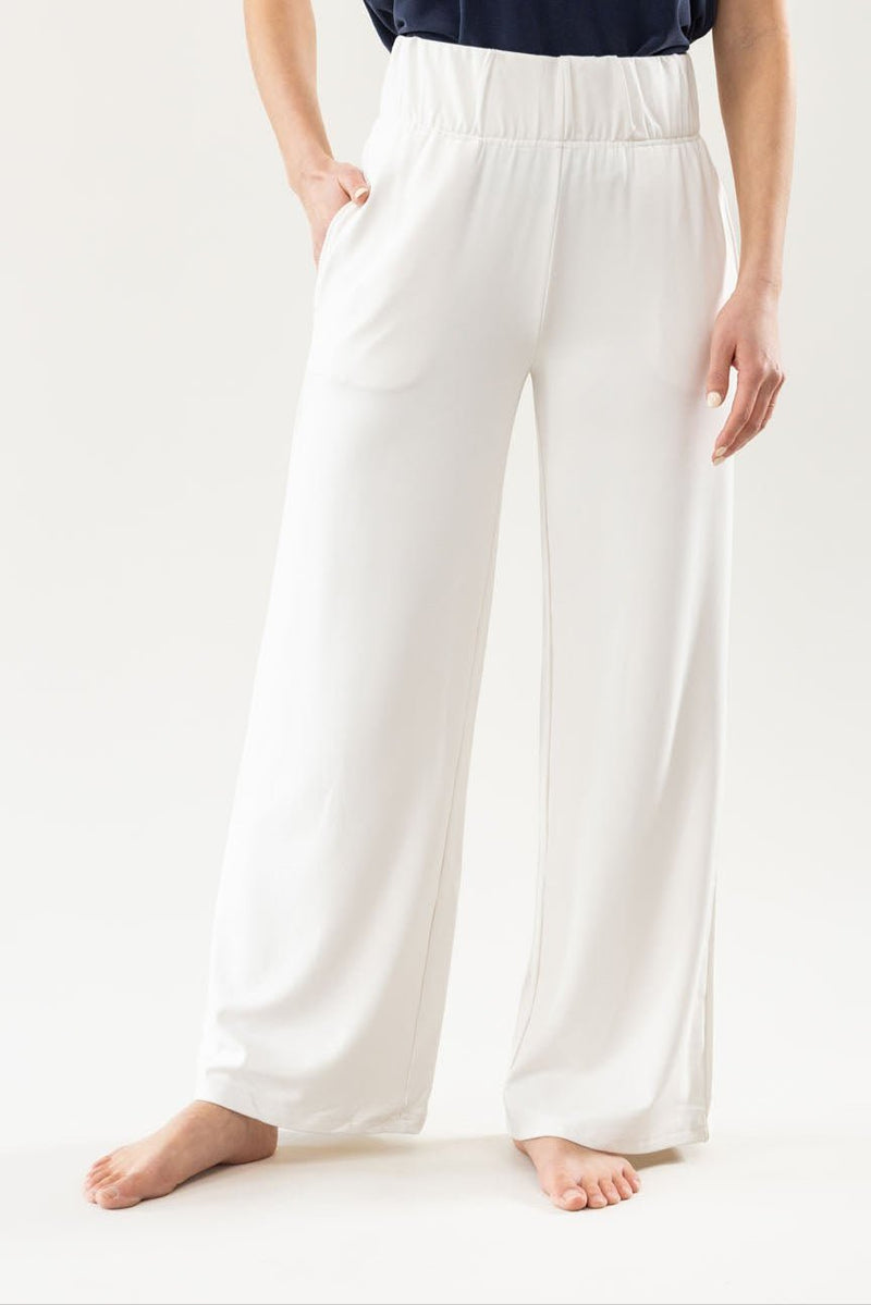 On a light background, someone wears Cozy Earth's Women's Ultra-Soft Bamboo Wide Leg Pull On Pant & Pullover Set in navy blue, featuring white wide-legged pants with an elastic waistband. The person is barefoot, with one hand in a pocket.