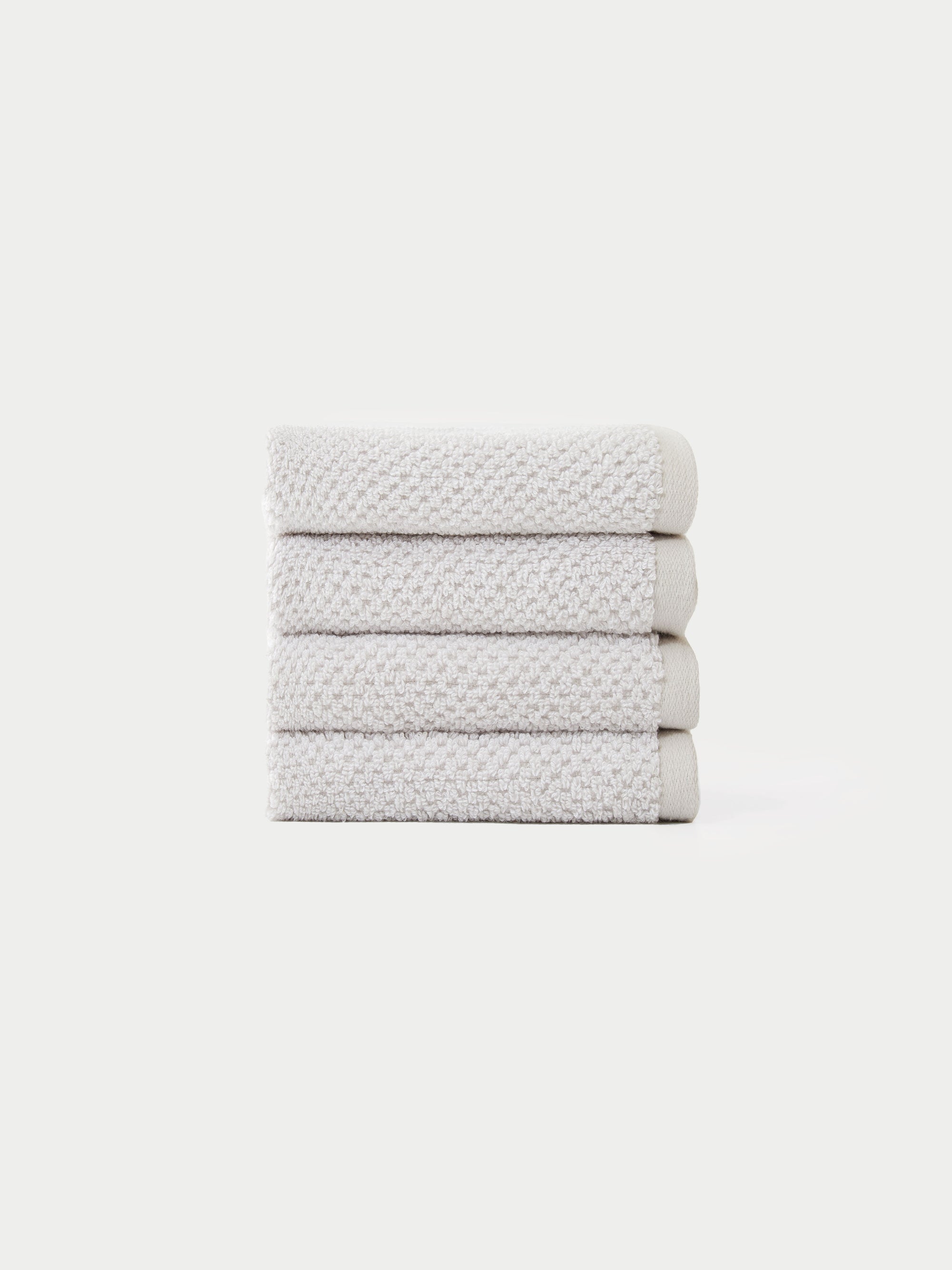 A neatly stacked pile of four folded, light gray textured Nantucket Bath Towels by Cozy Earth is set against a plain white background.