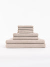 The Cozy Earth Nantucket Bath Towel Set features beige textured towels in various sizes, neatly stacked from largest to smallest, set against a plain white background.|Color:Heathered Sand
