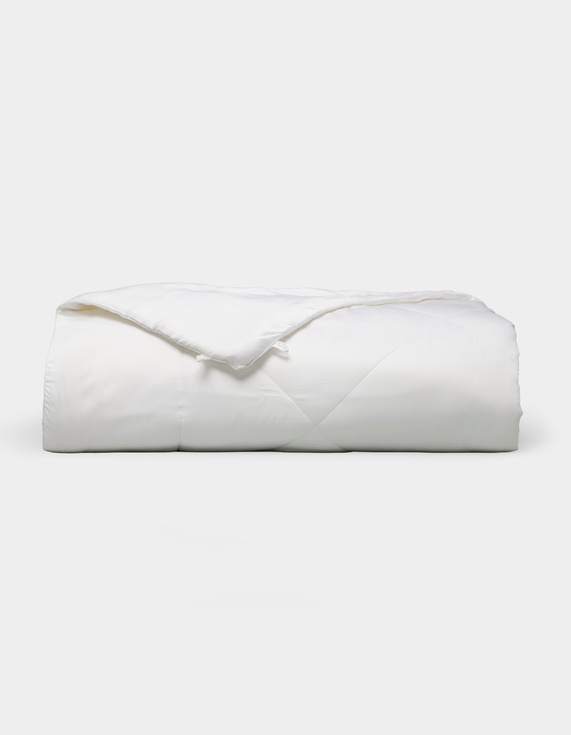 The Bamboo Viscose All Season Comforter by Cozy Earth, featuring a neatly folded white design with a subtle sheen, is displayed against a plain light background.