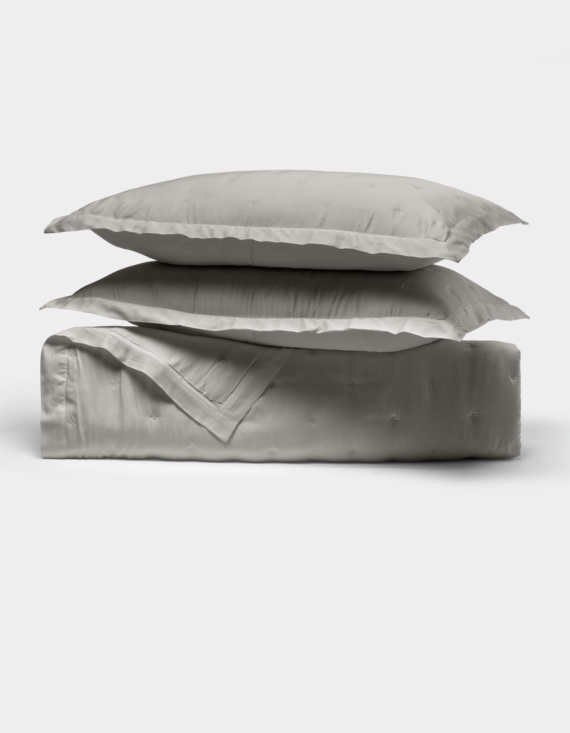 The Cozy Earth Bamboo Quilt Bundle features two light gray pillows stacked atop a folded matching comforter, all crafted from smooth, shiny fabric, displayed against a plain white background.|Color:Light Grey