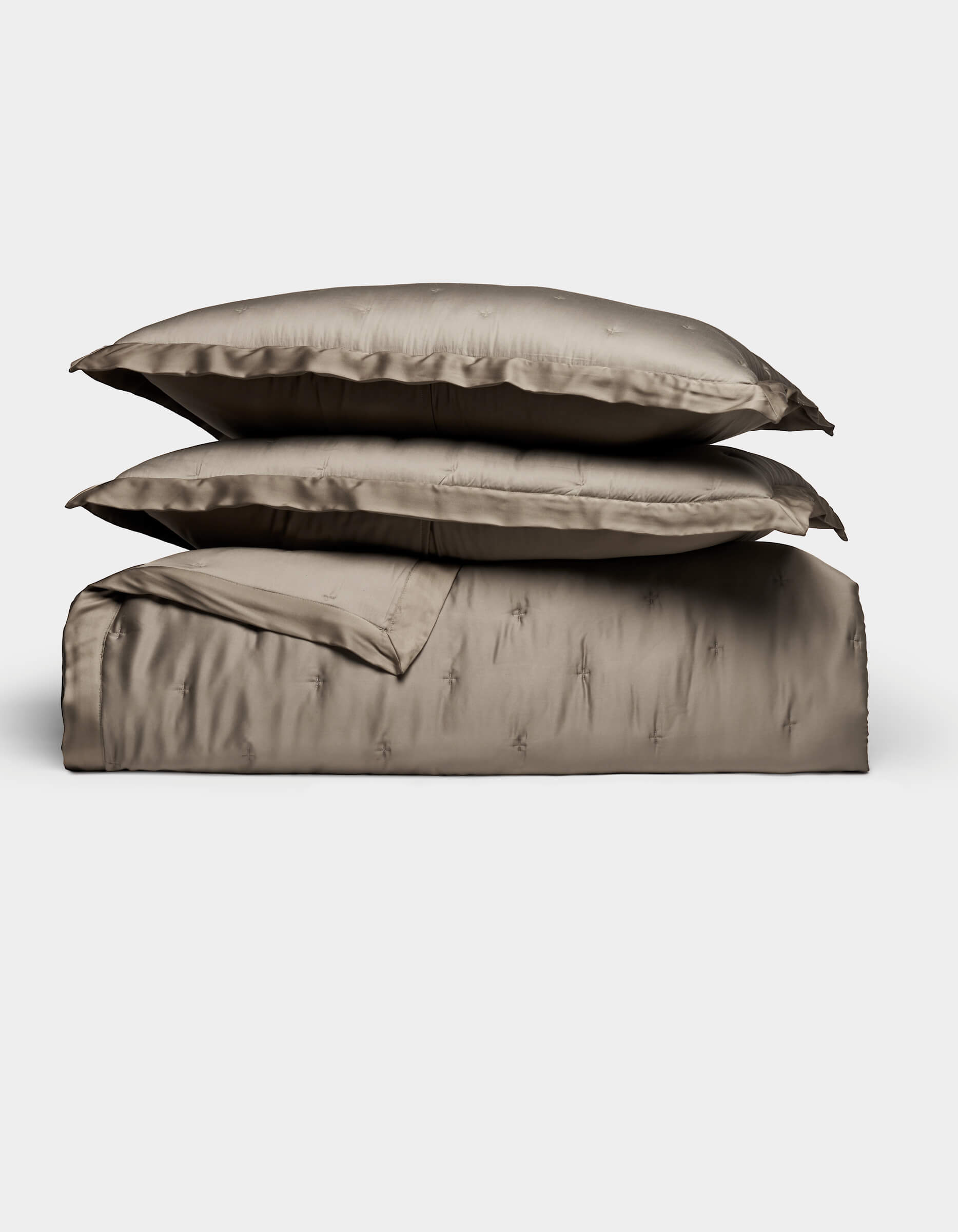 The Cozy Earth Bamboo Quilt Bundle features two plush pillows and a folded, shiny taupe duvet, all neatly arranged against a plain white background.|Color:Walnut