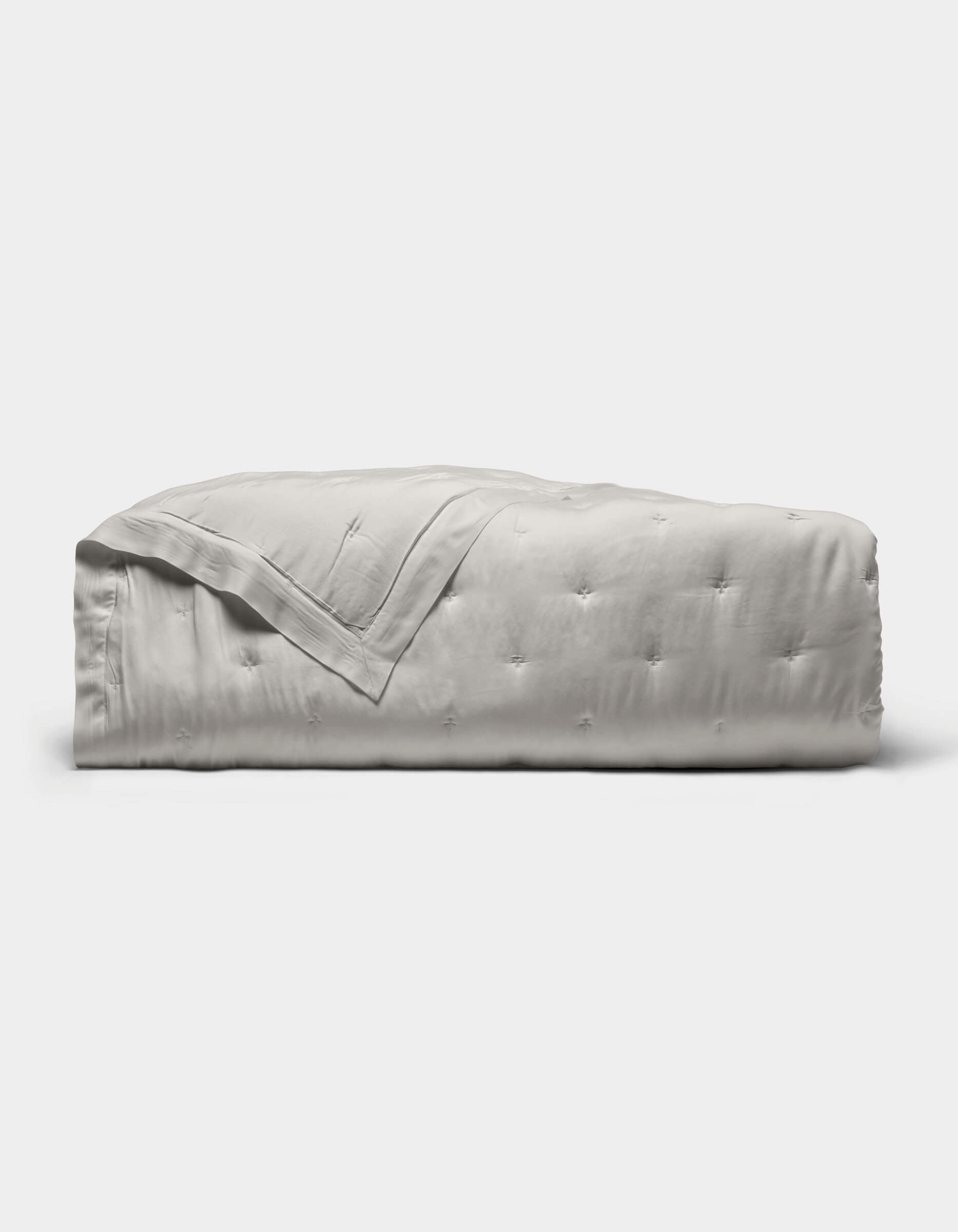 The Cozy Earth Bamboo Quilt, featuring a subtle tufted pattern and light gray color, is neatly folded against a plain white background.