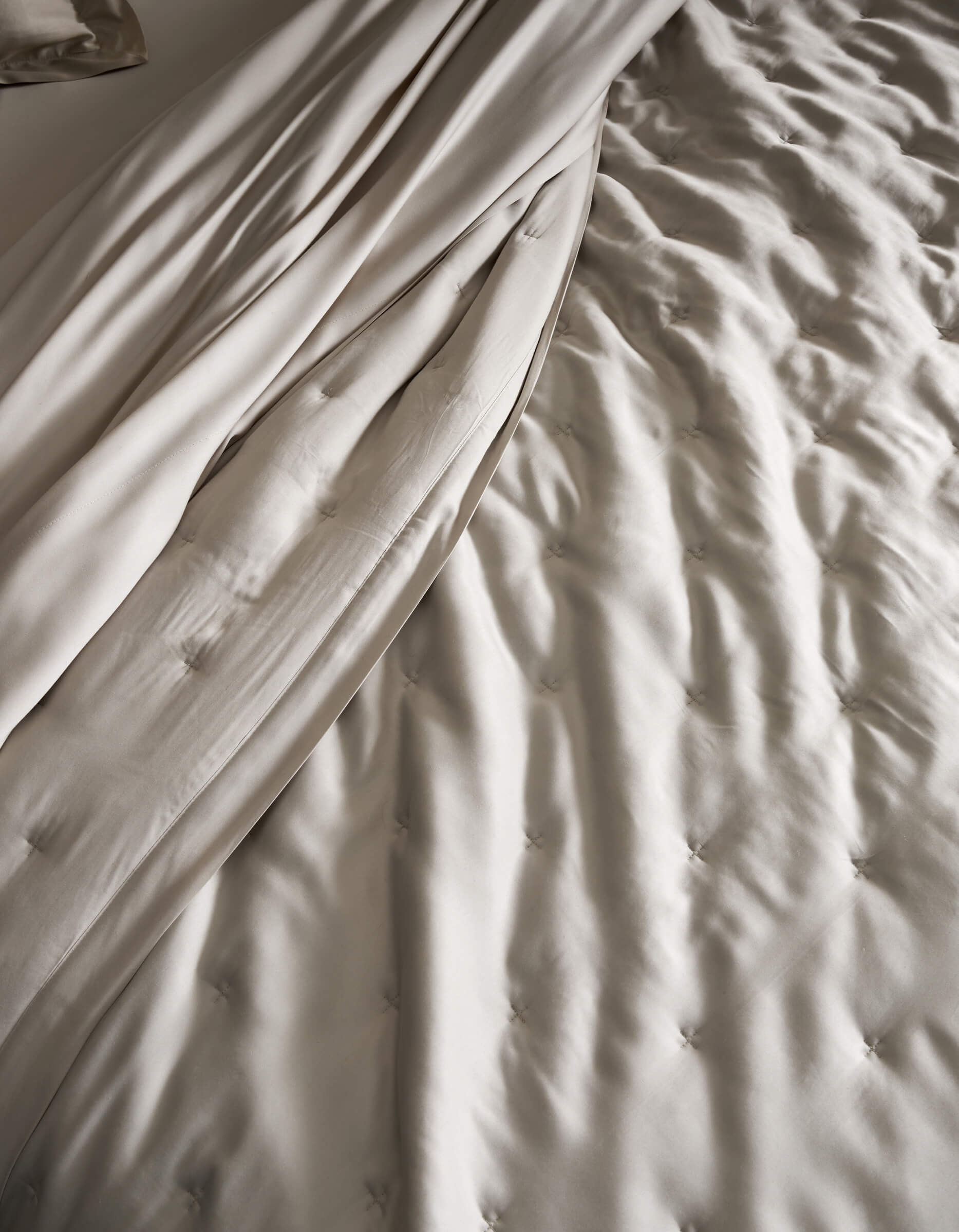A close-up of a neatly made bed featuring the Cozy Earth Bamboo Quilt, showcasing its light beige, tufted design and smooth, draped sheets for a soft and elegant texture.