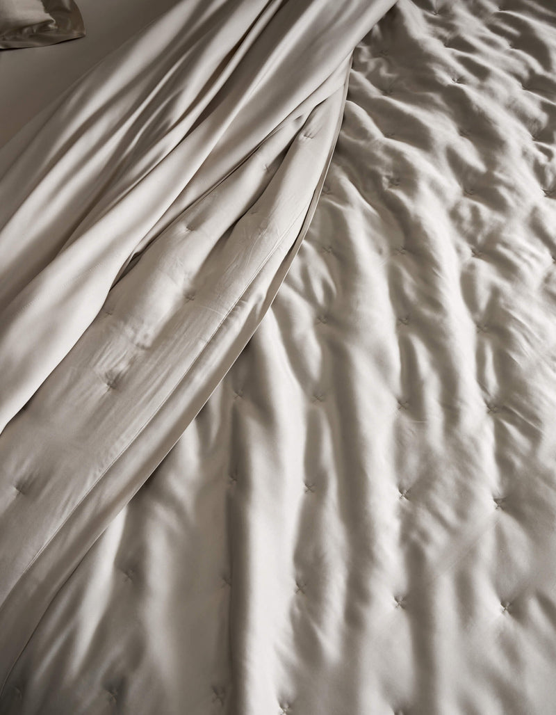 A close-up of a neatly made bed featuring the Cozy Earth Bamboo Quilt, showcasing its light beige, tufted design and smooth, draped sheets for a soft and elegant texture.