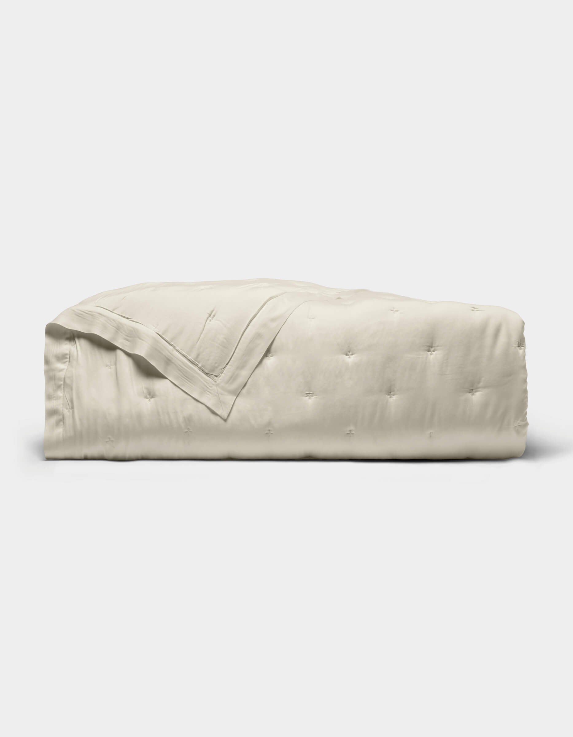 The Cozy Earth Bamboo Quilt, featuring a subtle quilted pattern and light beige color, is neatly folded and displayed against a plain white background.