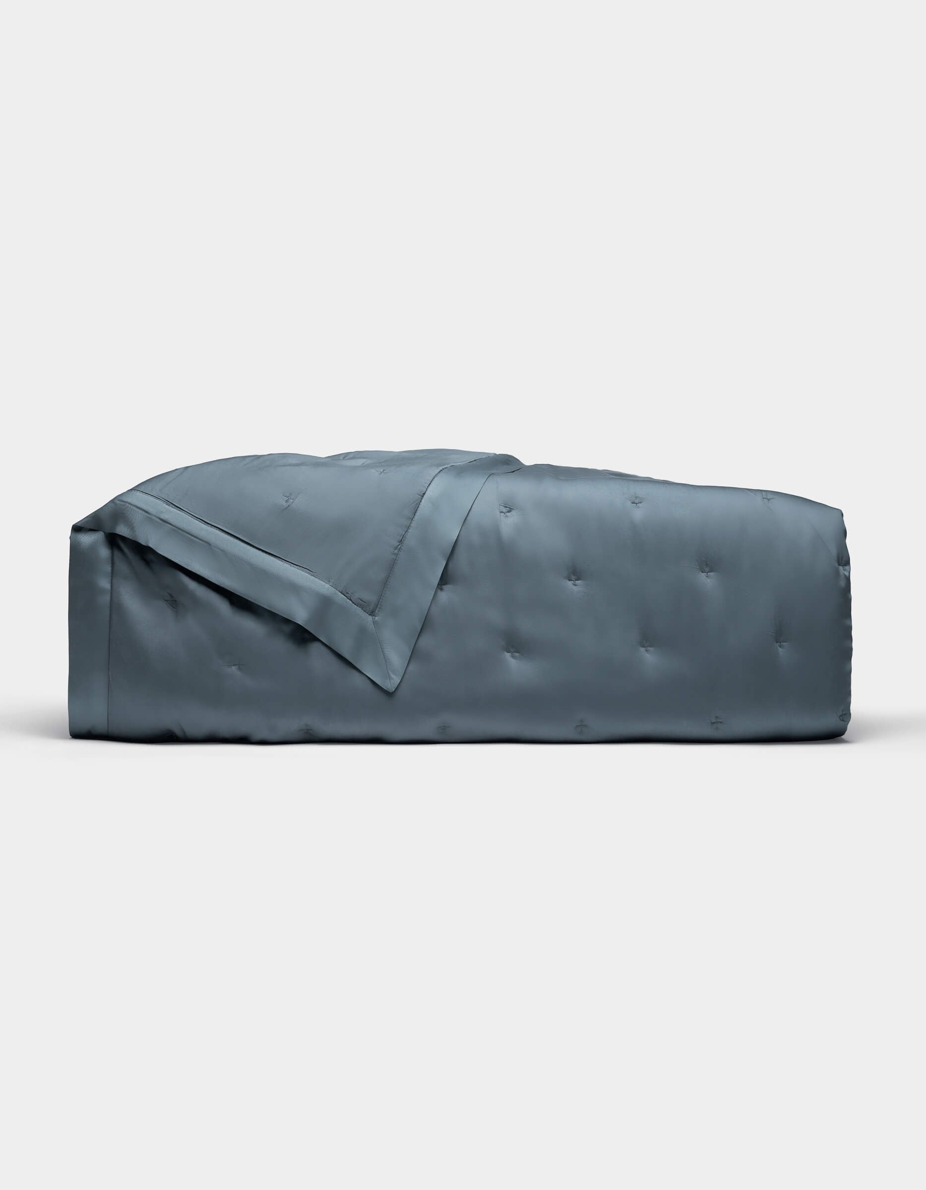 The Cozy Earth Bamboo Quilt, shown folded against a plain white background, features a blue-gray color with a subtle quilted pattern and smooth, shiny finish.|Color:Pacific Blue