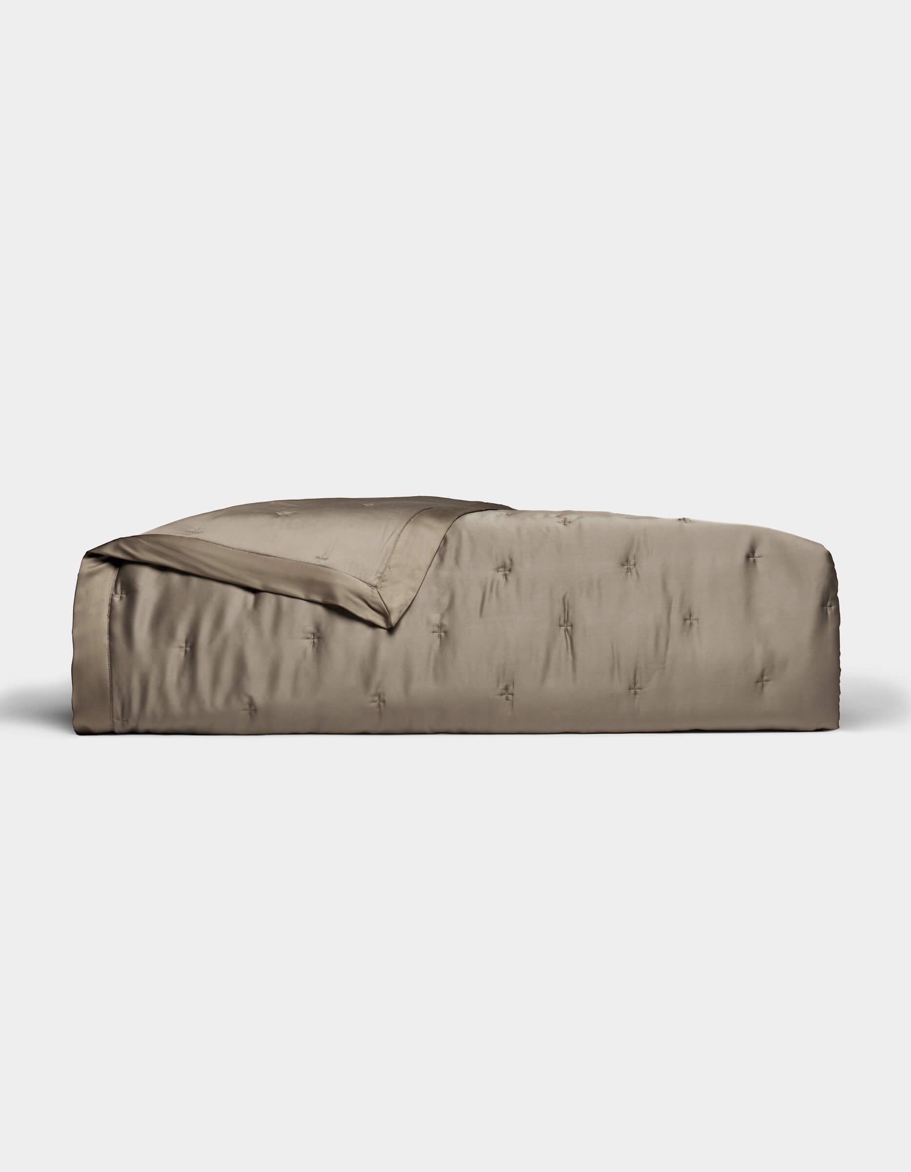 A neatly made bed with a smooth, shiny taupe Cozy Earth Bamboo Quilt and matching blanket partially folded back, set against a plain white background.