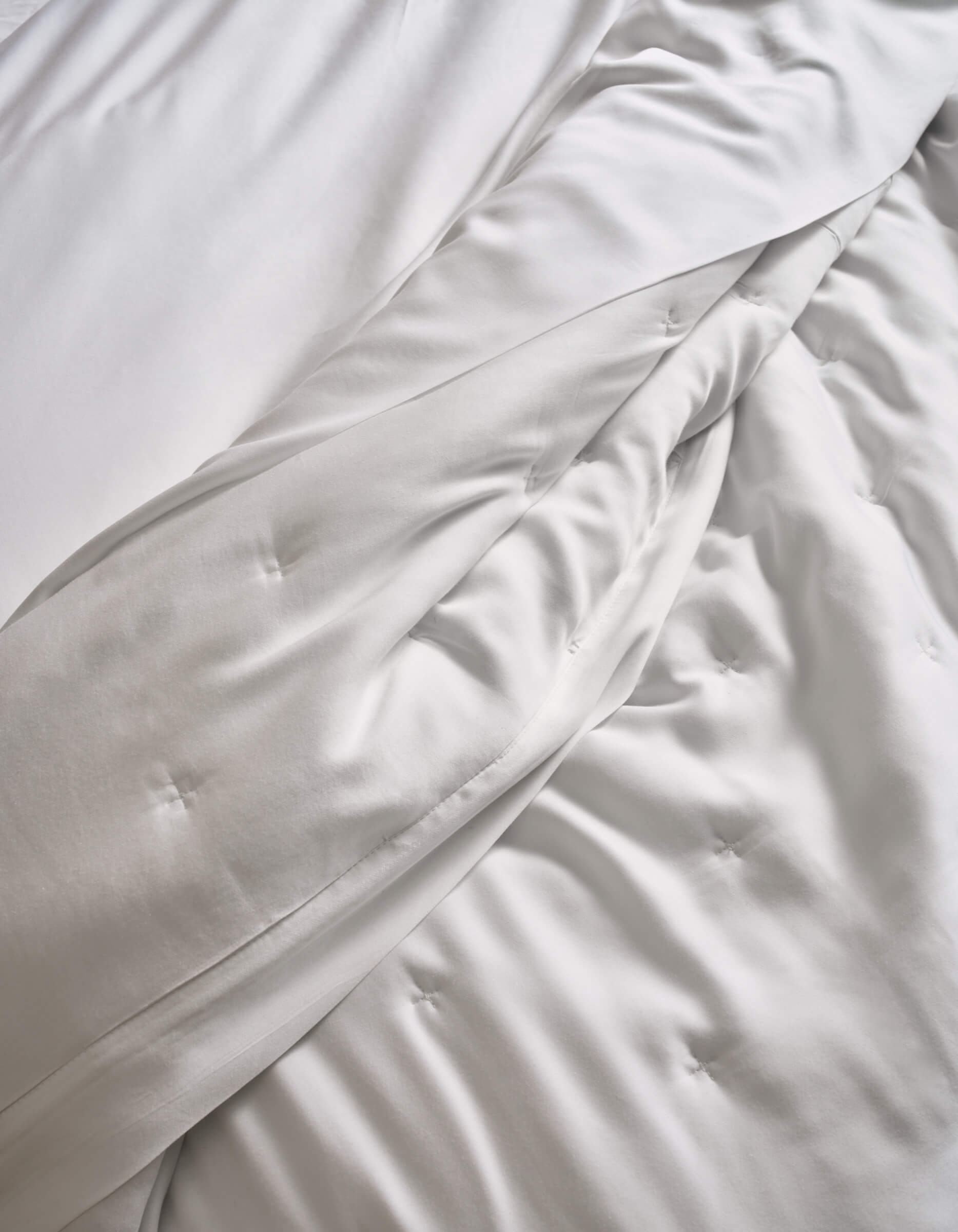 Close-up of a neatly made bed featuring Cozy Earth’s Bamboo Quilt, with soft, white, slightly wrinkled sheets and the plush, quilted comforter creating a cozy and inviting look.