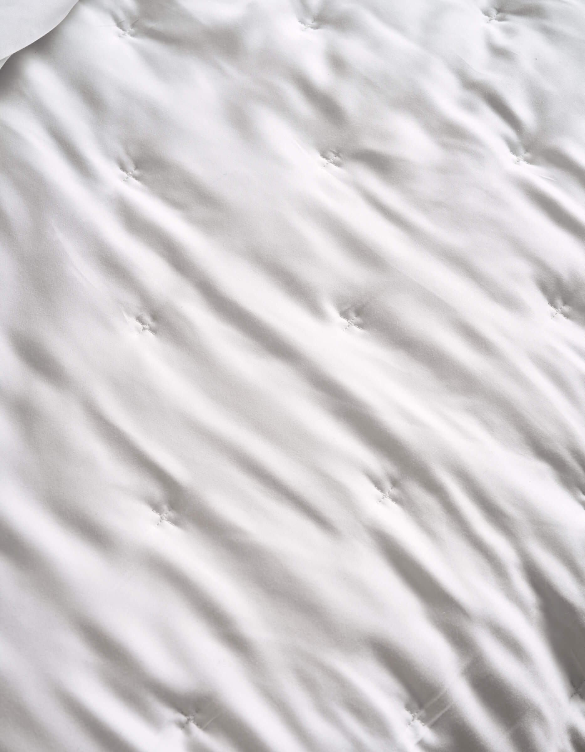 A close-up of the Cozy Earth Bamboo Quilt’s white, tufted surface features gentle waves and sewn dimples, hinting at its soft, quilted texture.