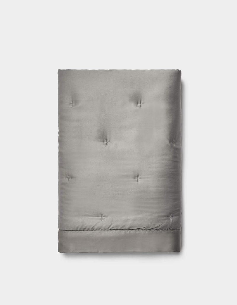 The Cozy Earth Bamboo Quilted Shams in light gray feature a smooth, slightly shiny surface with subtle tufted details, neatly folded and set against a plain white background.