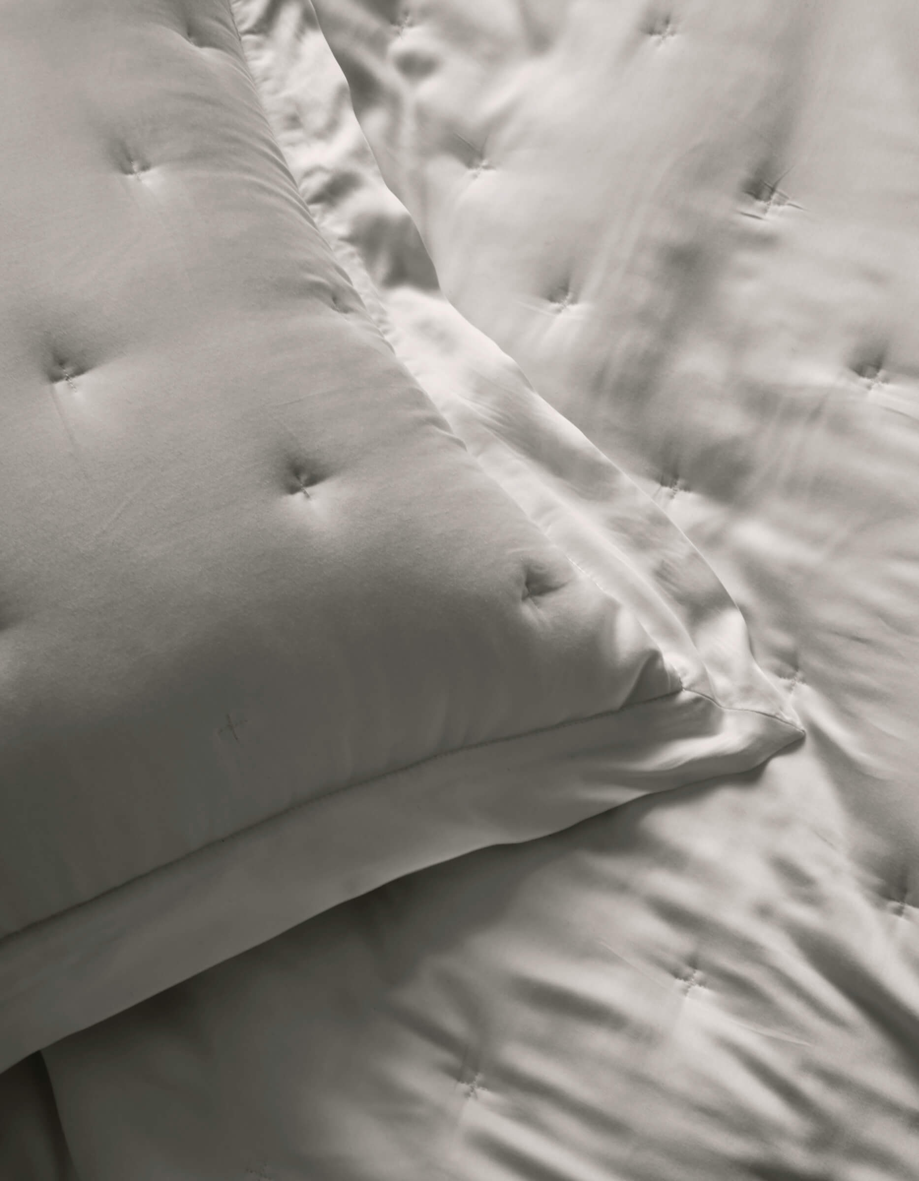 Close-up of two Cozy Earth Bamboo Quilted Shams and a matching comforter, all in smooth, light gray satin fabric with a subtle sheen.