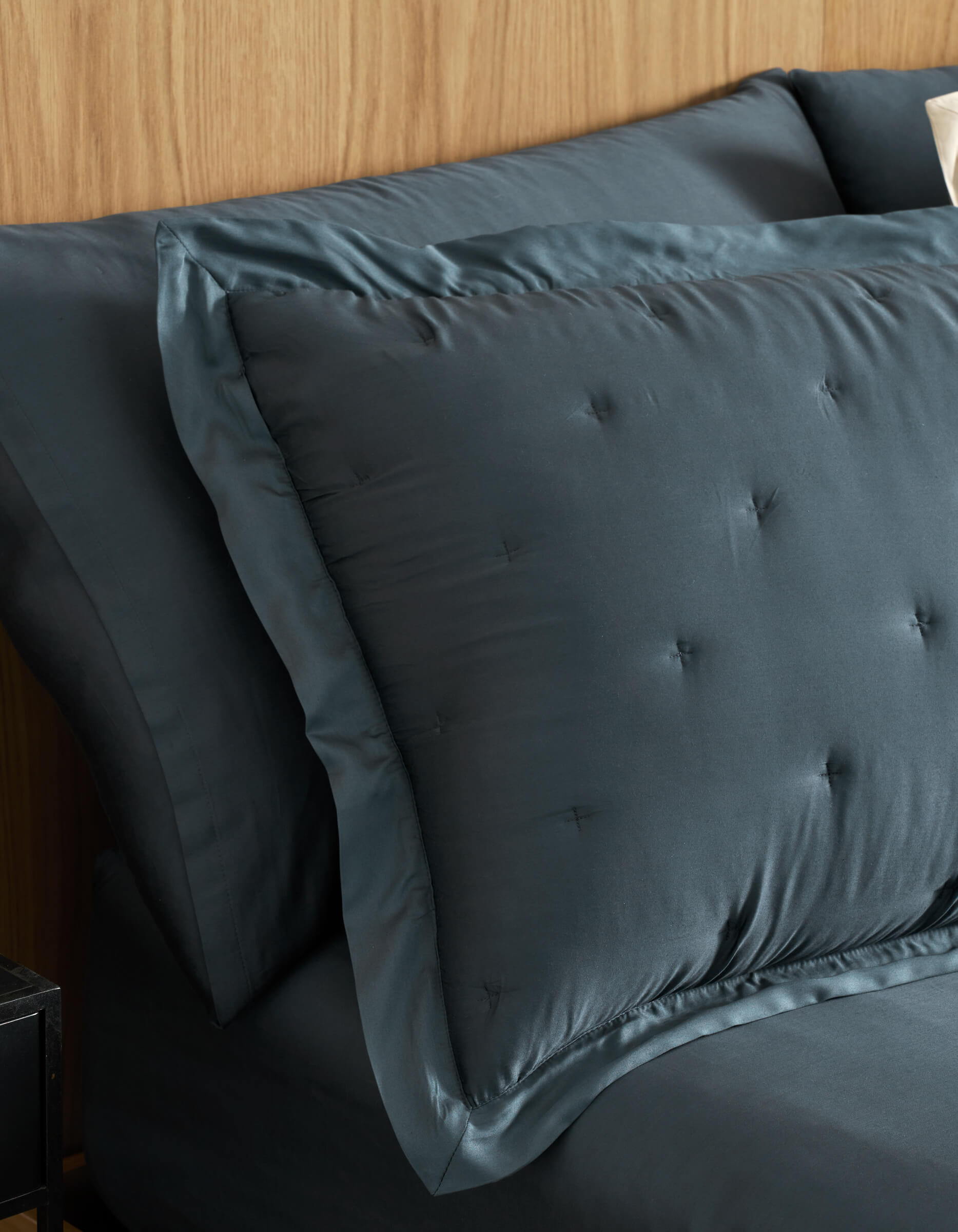 A close-up of a neatly made bed features Cozy Earth Bamboo Quilted Shams and matching sheets in dark blue, set against a light wood headboard.|Color:Pacific Blue