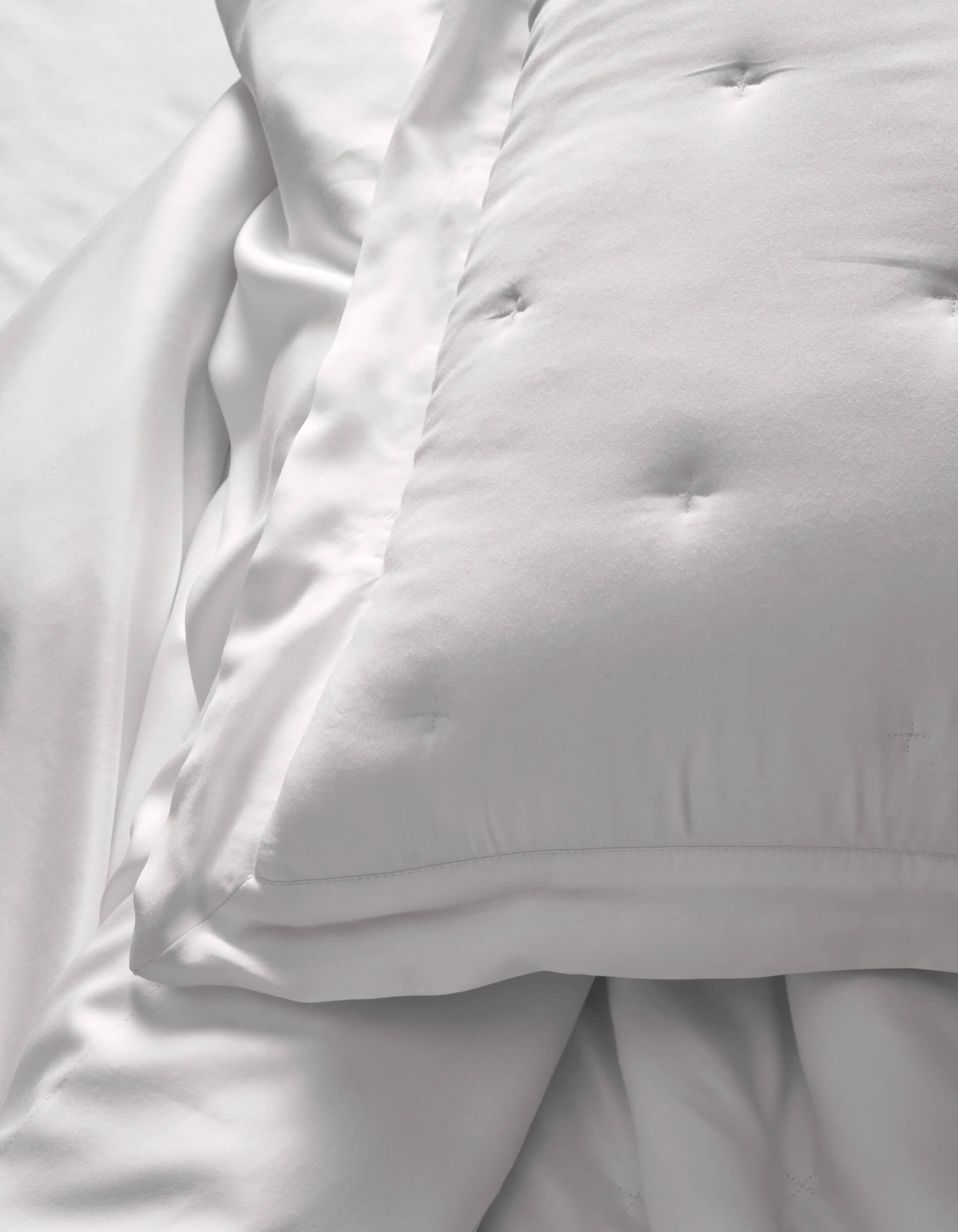 A close-up of Cozy Earth Bamboo Quilted Shams resting on smooth white sheets creates a soft, clean look. The bedding appears fluffy and inviting.