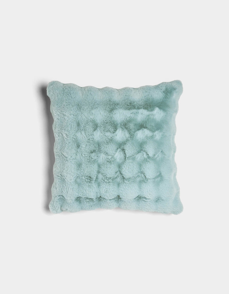 The Bubble Cuddle Pillow by Cozy Earth is a square, light blue faux fur pillow with a wavy texture and scalloped edges, displayed against a white background.