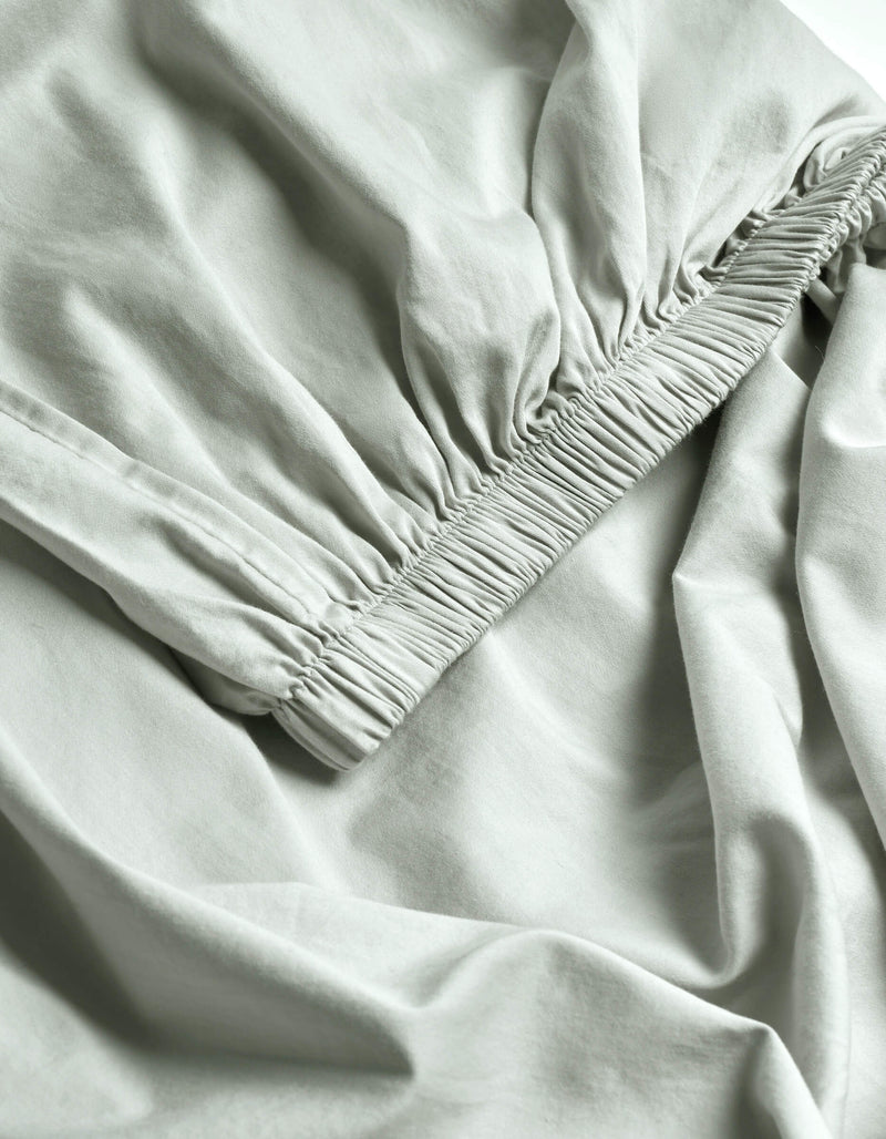 Close-up of Cozy Earth's Soft-Wash Cotton Fitted Sheet in light gray, featuring ruched elastic edges that create gentle folds and a textured, smooth, and lightweight surface.