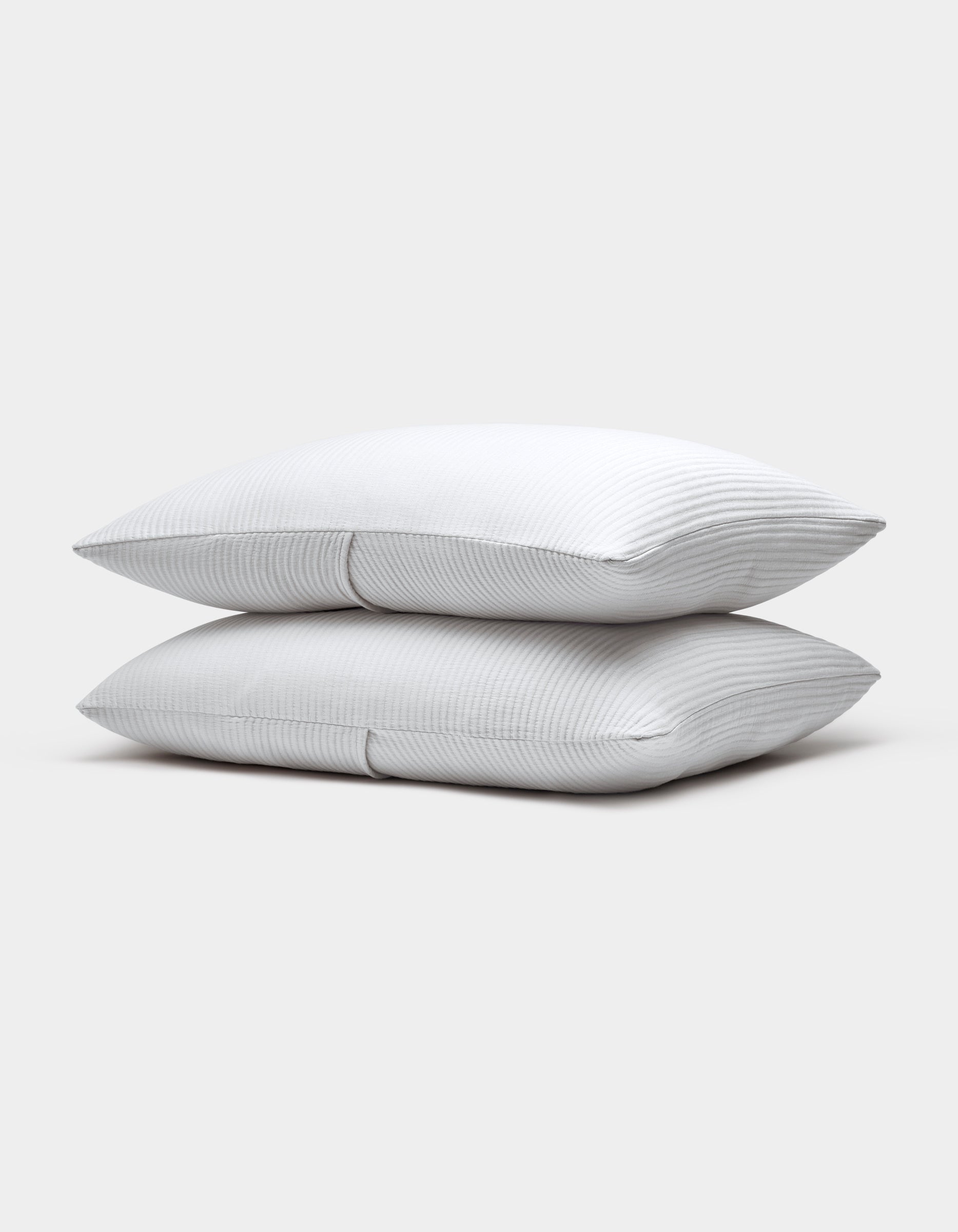 Two Cozy Earth Bamboo Coverlet Shams, white with subtle thin gray stripes, are stacked neatly atop each other against a plain light gray background.|Color:White