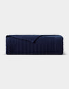 The Cozy Earth Bamboo Coverlet, in dark navy blue with a ribbed texture and one corner turned down, is displayed neatly against a plain light gray background.|Color:Navy