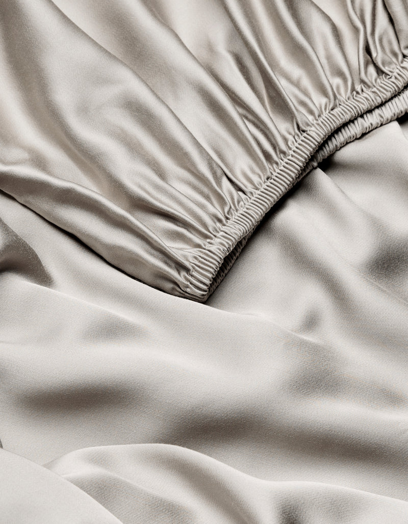 Close-up of Cozy Earth Bamboo Fitted Sheet in light beige, highlighting its smooth, shiny texture with gentle folds and ruching near the seam.