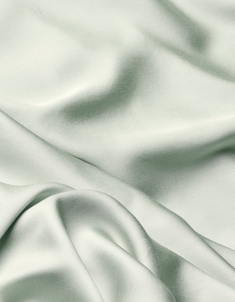 The Cozy Earth Bamboo Flat Sheet features a soft, light sage green fabric with a smooth texture and gentle folds that create subtle shadows and highlights across its surface.