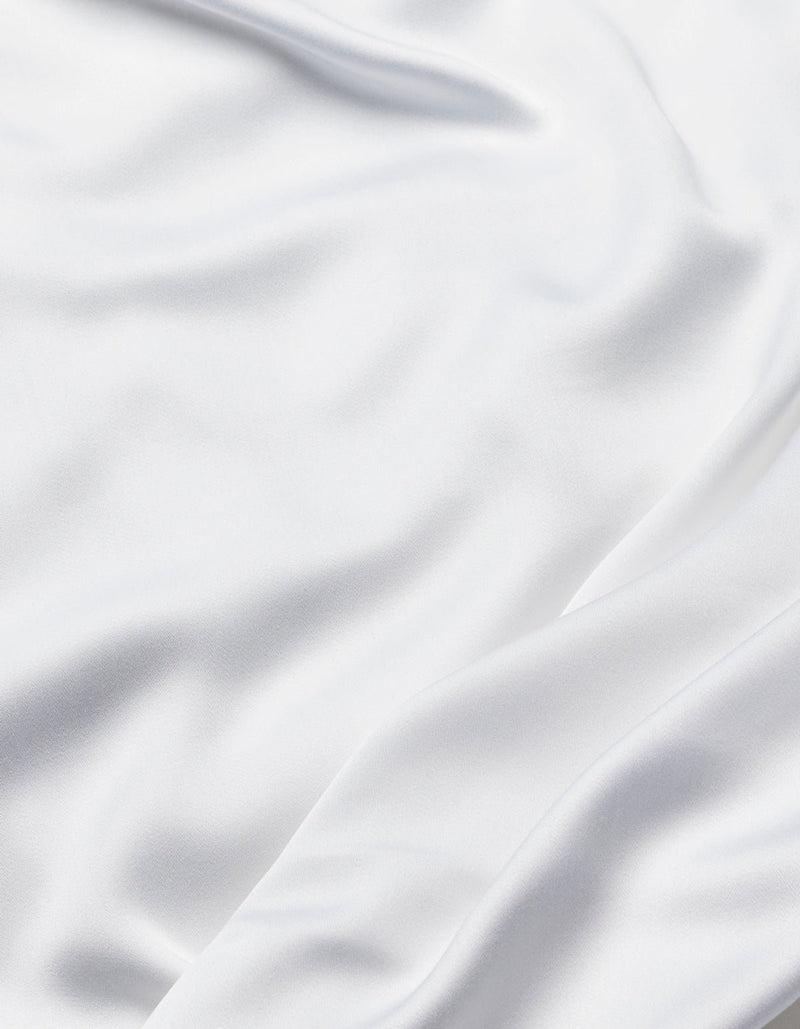 The Cozy Earth Bamboo Sheet Set features smooth white fabric with soft folds and flowing creases, offering a silky, elegant texture.