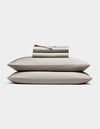 The Cozy Earth Bamboo Sheet Set, in light gray, includes neatly folded bed sheets and pillowcases stacked atop two pillows, all shown against a plain white background.|Color:Dove Grey