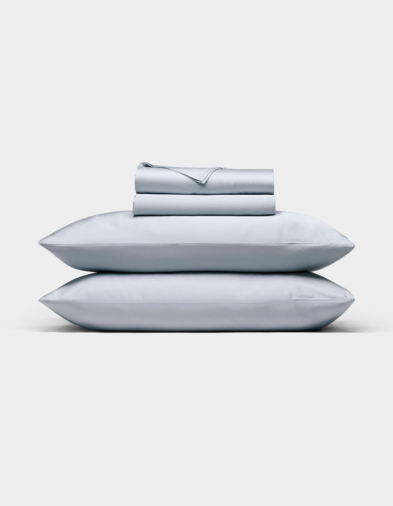 A neatly folded Cozy Earth Bamboo Sheet Set in light gray, with matching pillowcases stacked on two pillows, displayed against a plain white background.