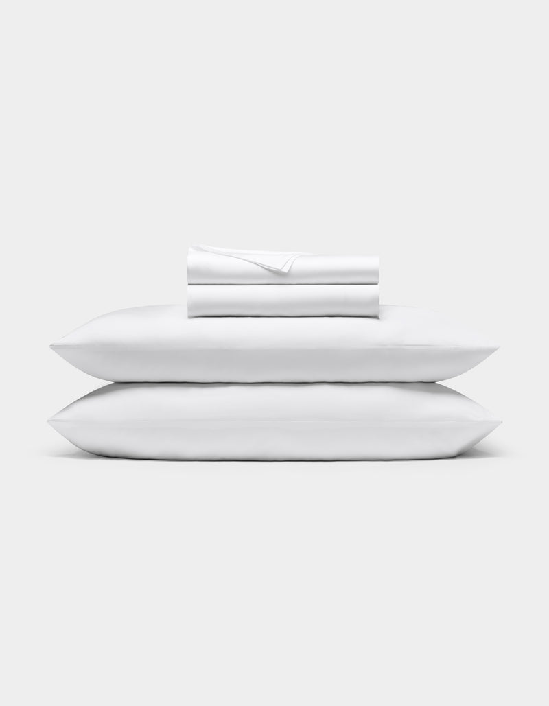 A neatly folded Bamboo Sheet Set by Cozy Earth is stacked on two white pillows, all set against a plain light gray background.