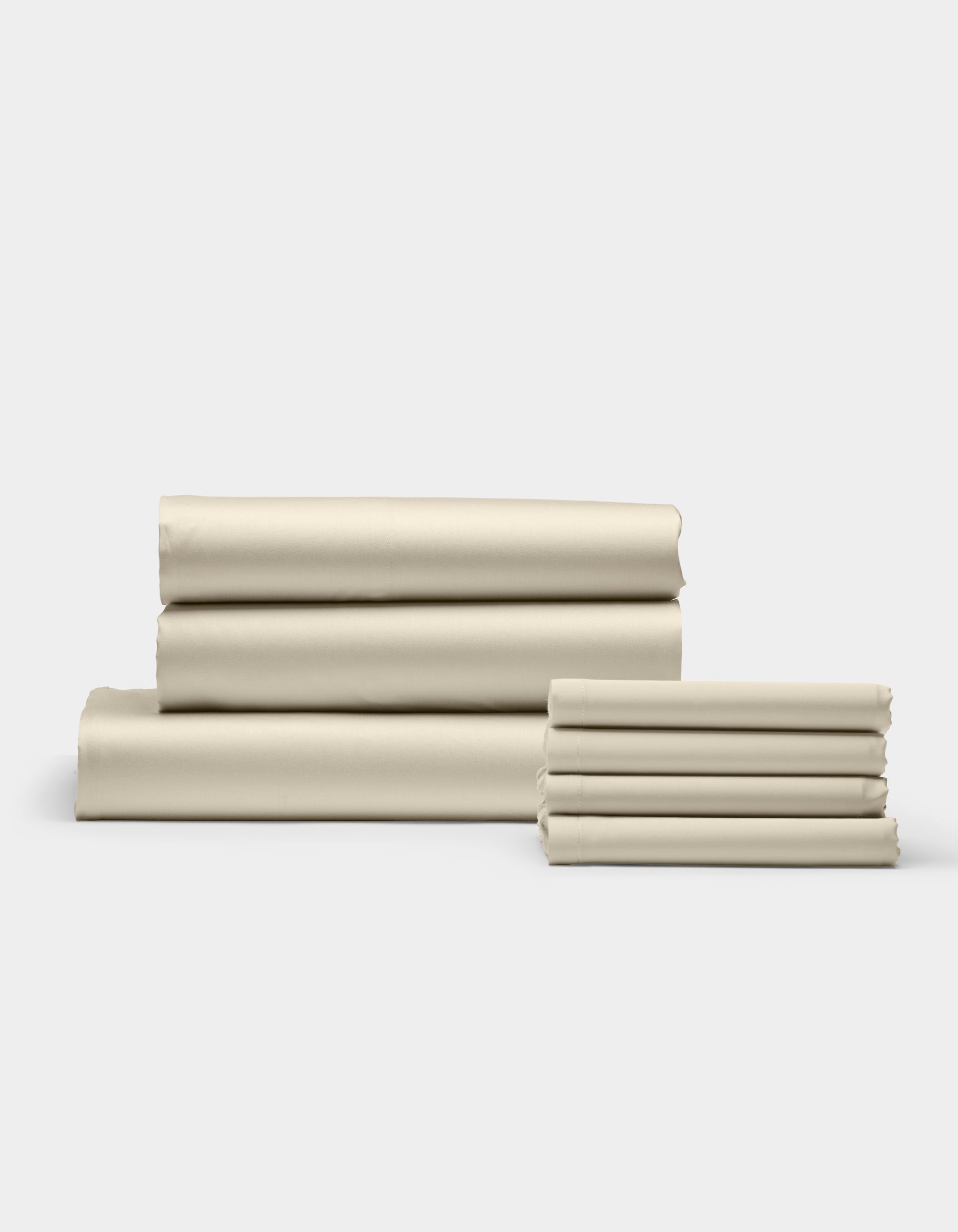 Cozy Earth’s Bamboo Bedding Core Bundle is shown in stacks of neatly folded beige sheets, arranged on a white surface with a light gray background. The smooth sheets are organized into one large and one small pile.