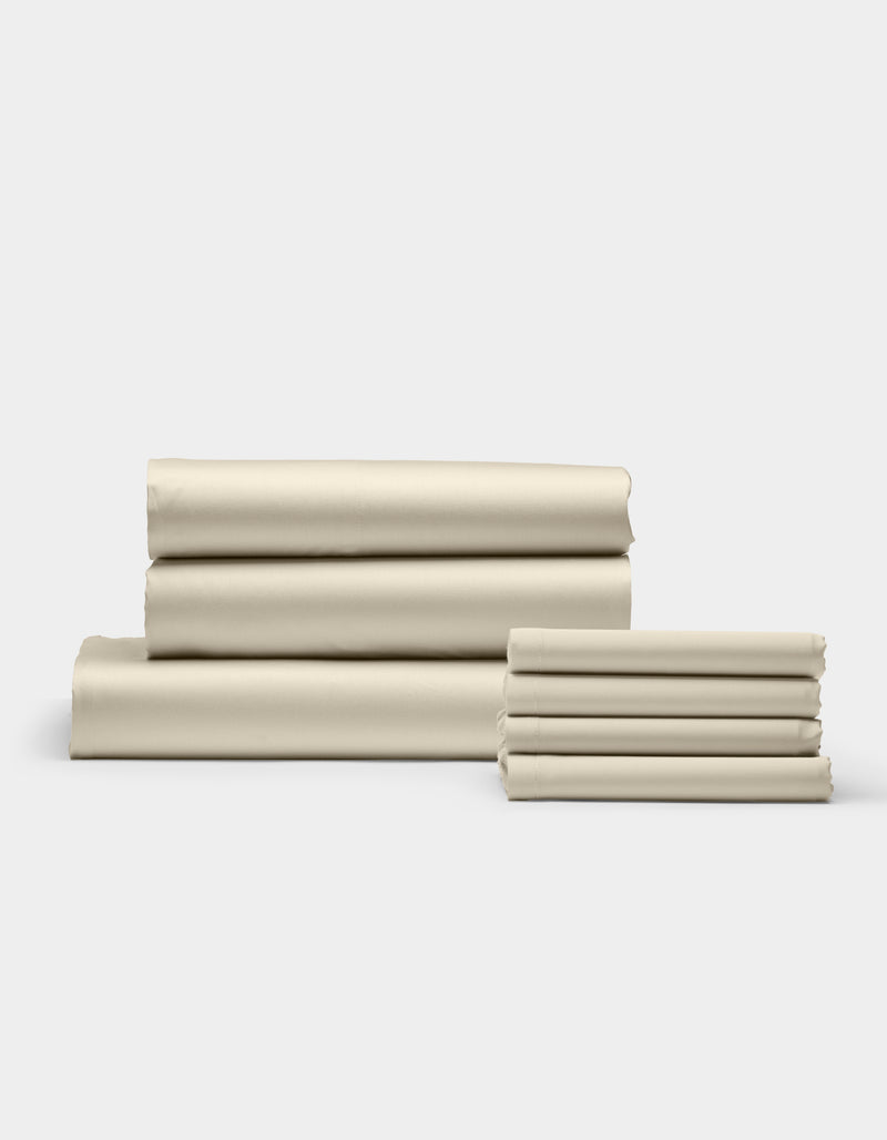 Cozy Earth’s Bamboo Bedding Core Bundle is shown in stacks of neatly folded beige sheets, arranged on a white surface with a light gray background. The smooth sheets are organized into one large and one small pile.
