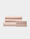 Cozy Earth’s Bamboo Bedding Core Bundle, shown in light pink, features neatly folded bed sheets and pillowcases arranged in two stacks against a simple, light background.|Color:Peony